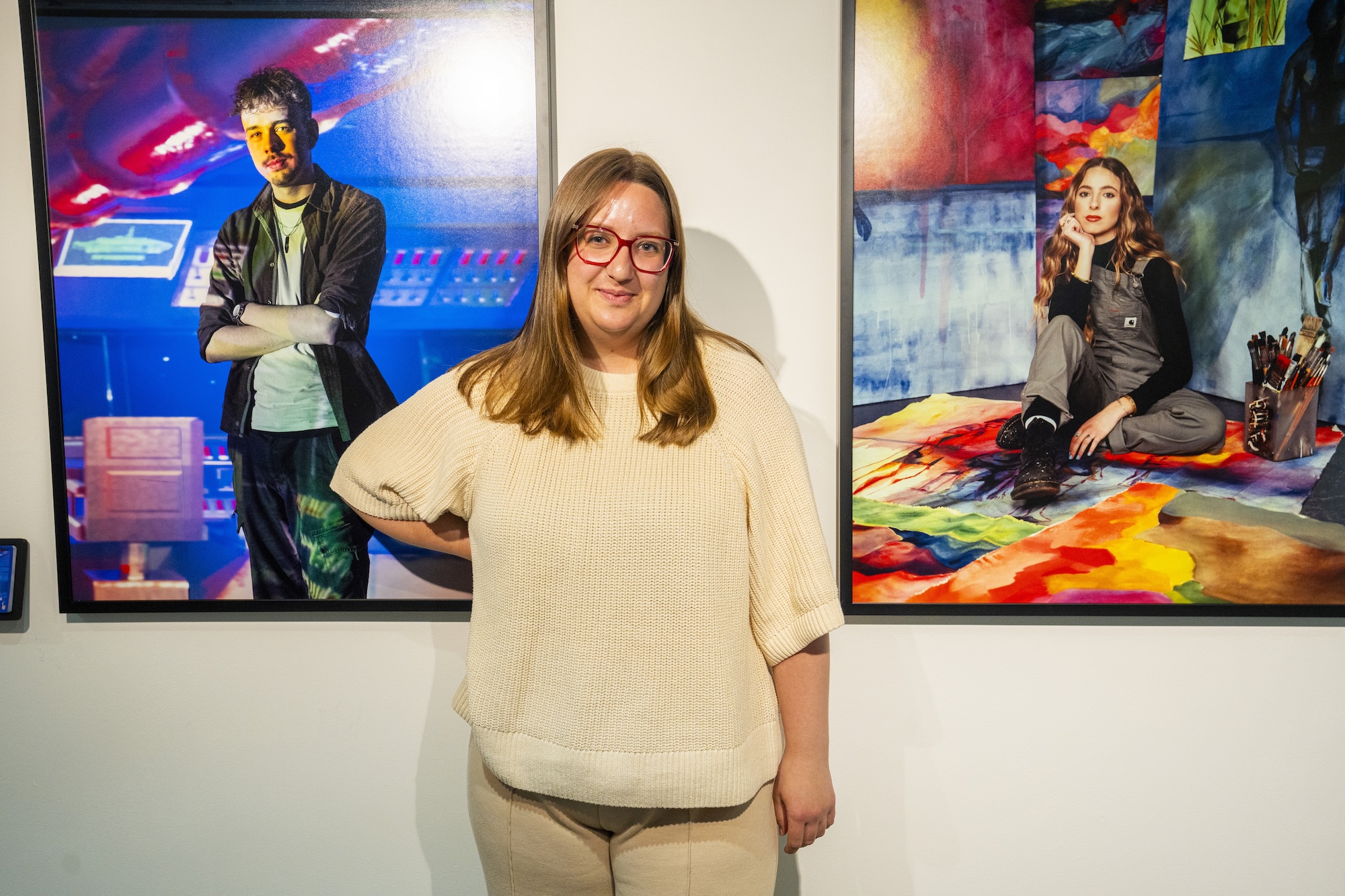 BA (Hons) Commercial Photography student R Virgo poses for a photo between two prints from the Arts University Bournemouth 2027 prospectus Archetypes deck.