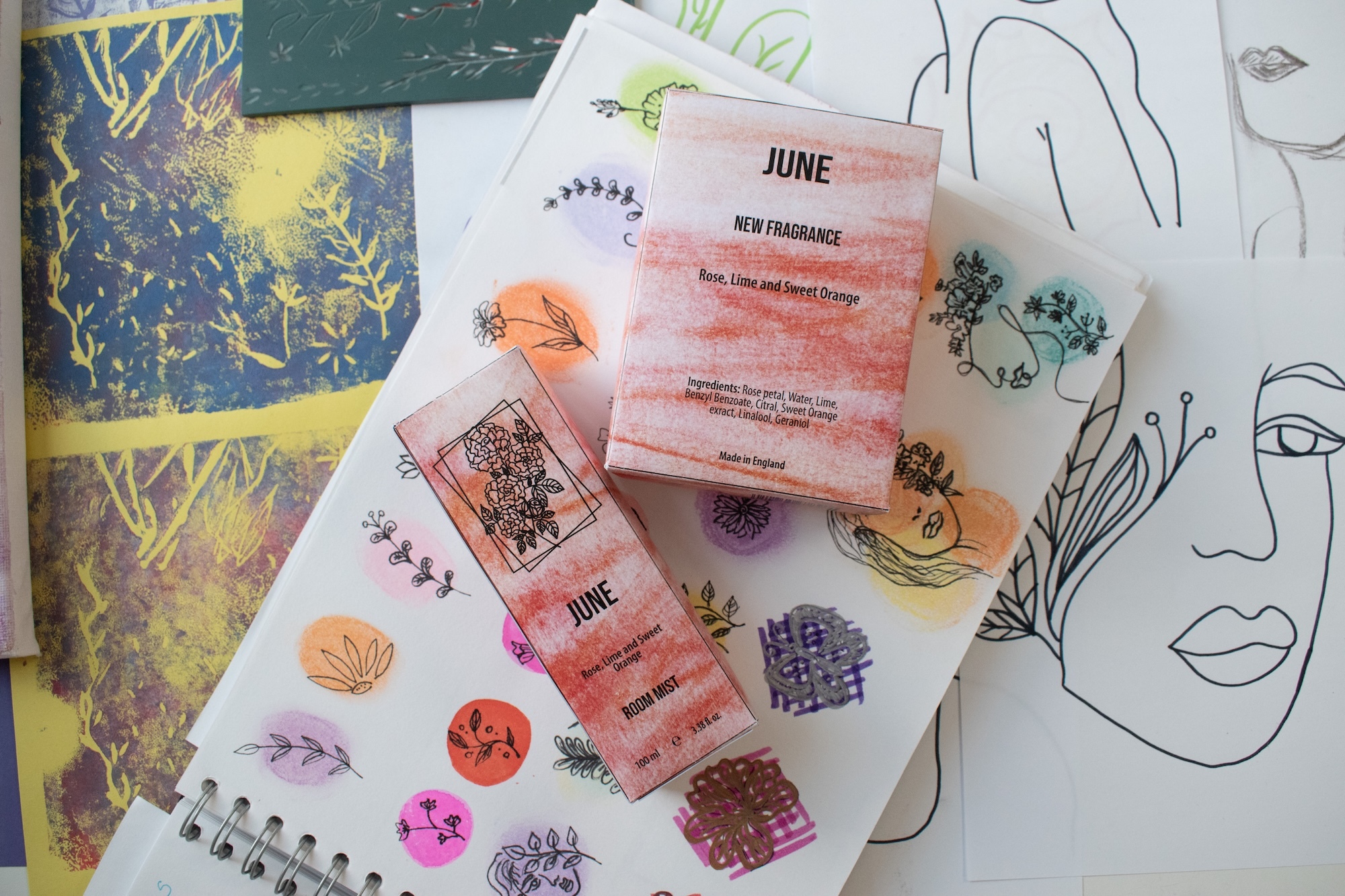 Scattered papers with pink watercolour blocks, botanical stamps, line drawings of faces, and yellow-green background elements on white surface.