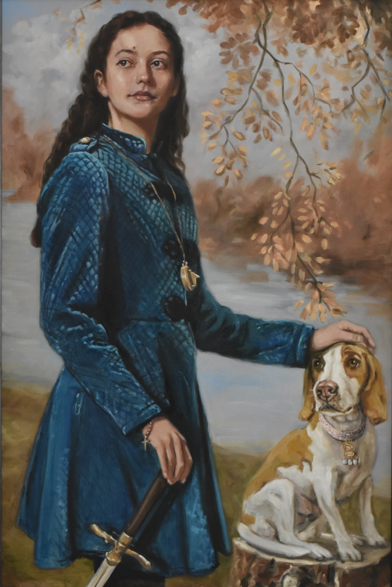 Portrait of a young woman in Medieval-style costume petting a dog and holding the pommel of a sword.
