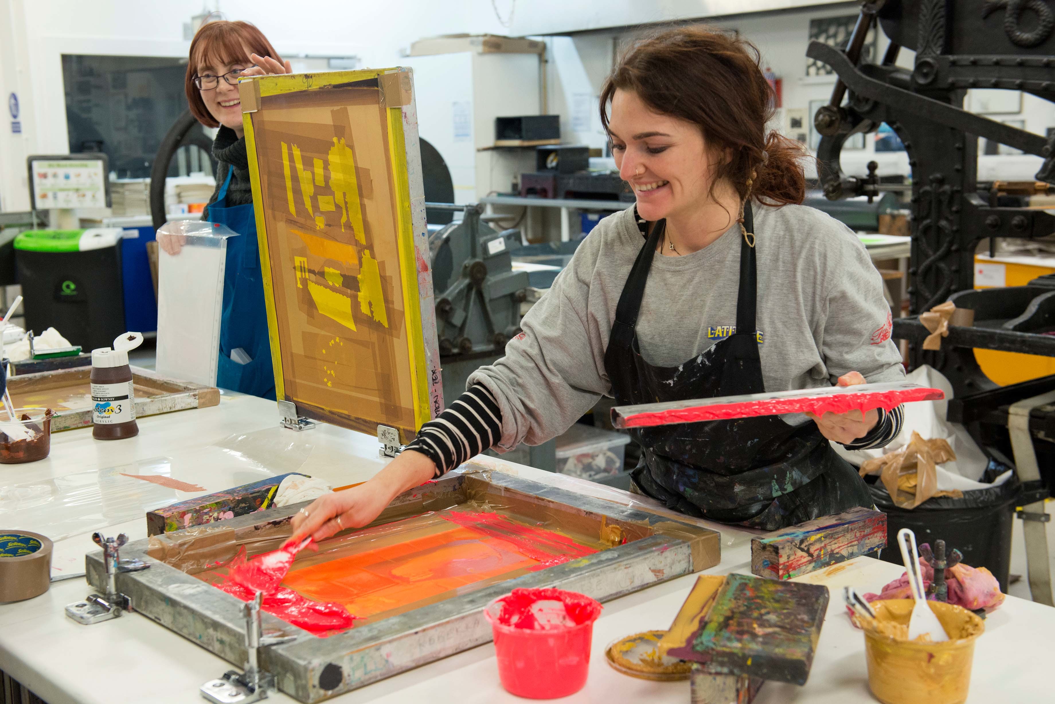 A student smiles as they put paint onto the screen to print.