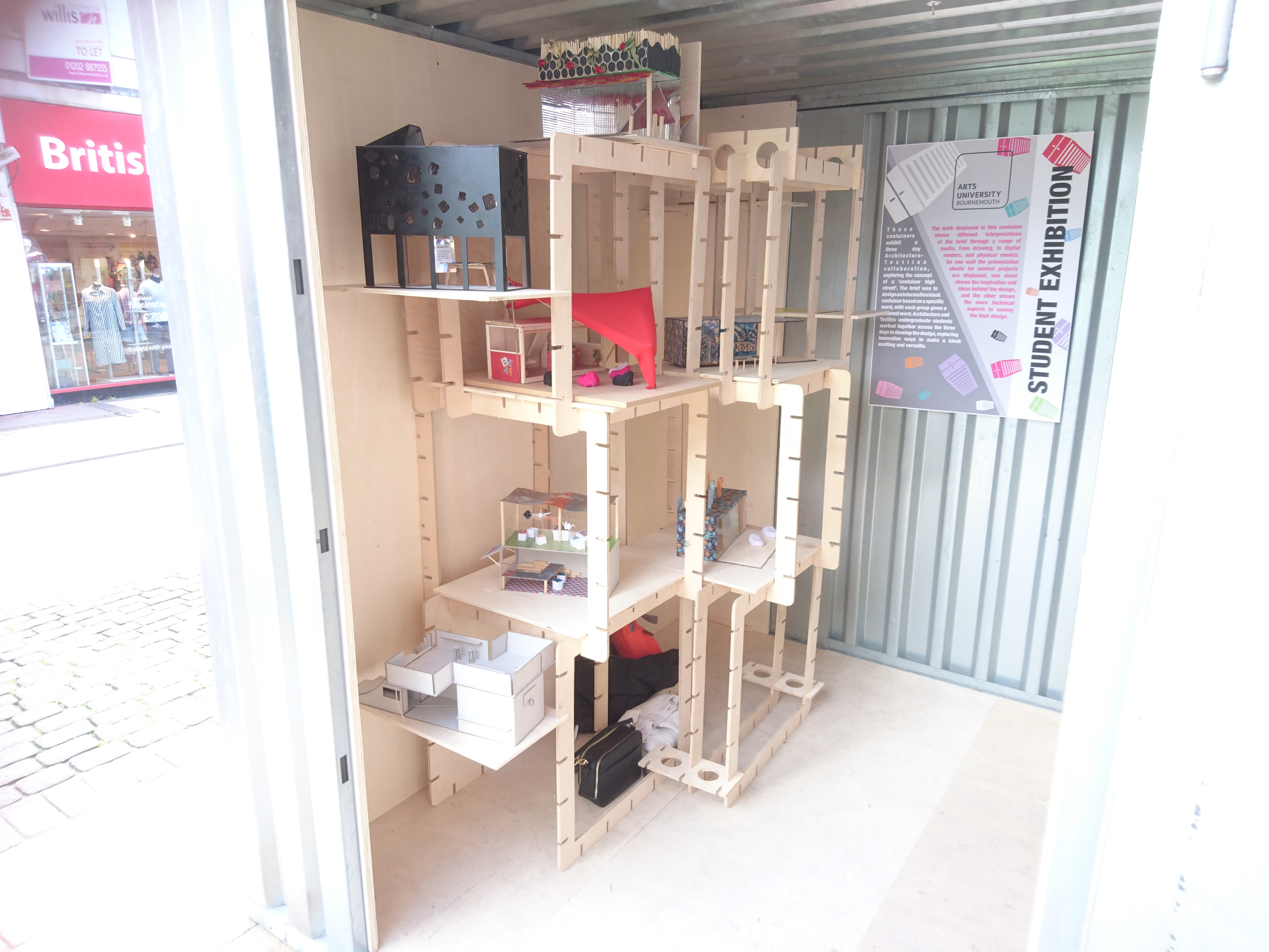 A set of model structures stands inside a metal shipping container on a high street.