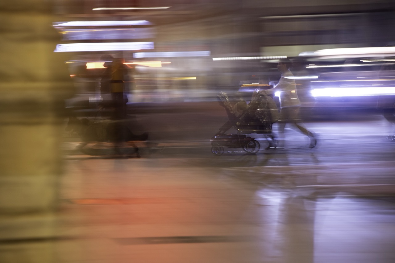 Blurred motion capture showing streaked lights in white, yellow, and purple against dark shapes on wet pavement.
