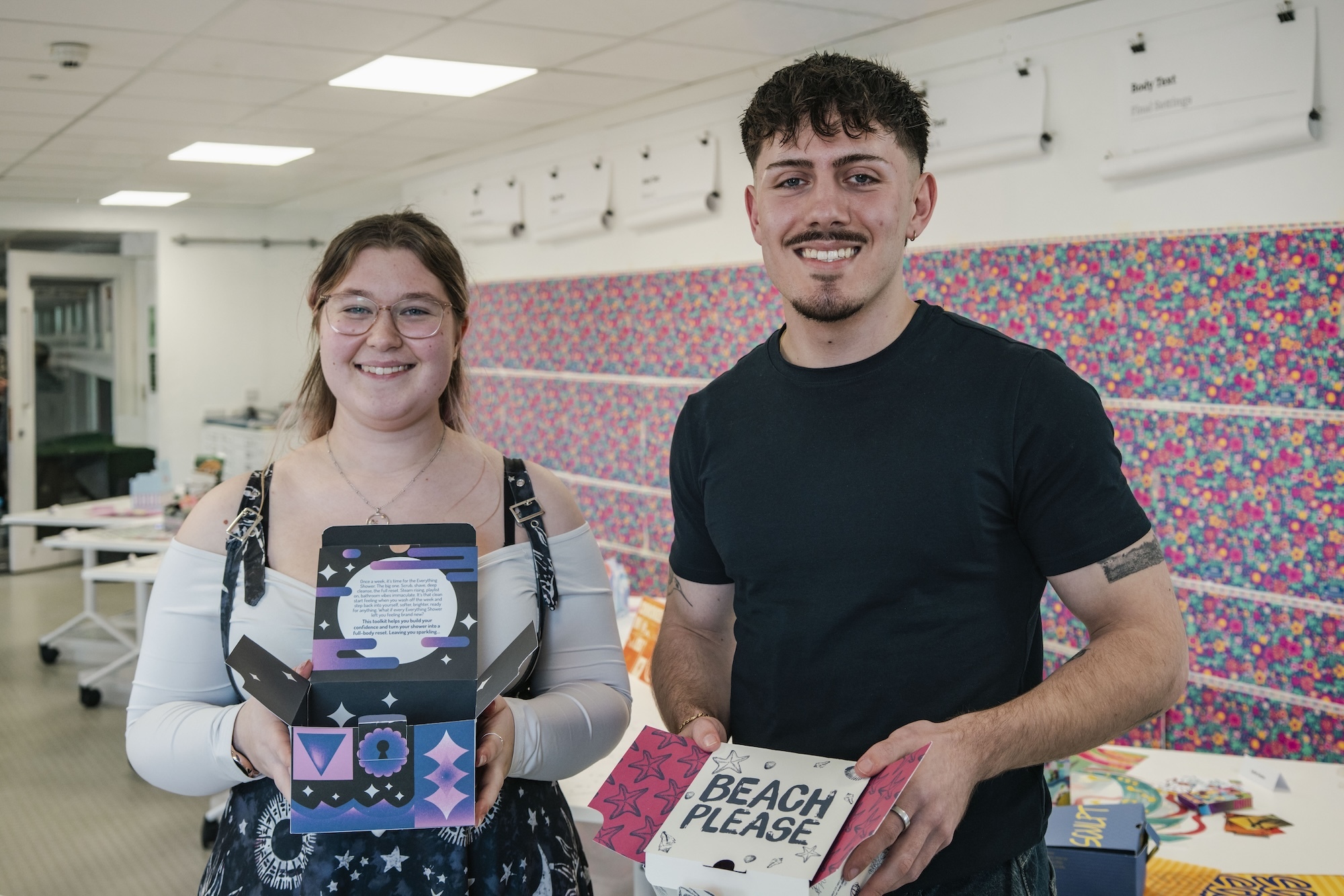 D Heywood and J Page holding packaging designs in a studio at Arts University Bournemouth.