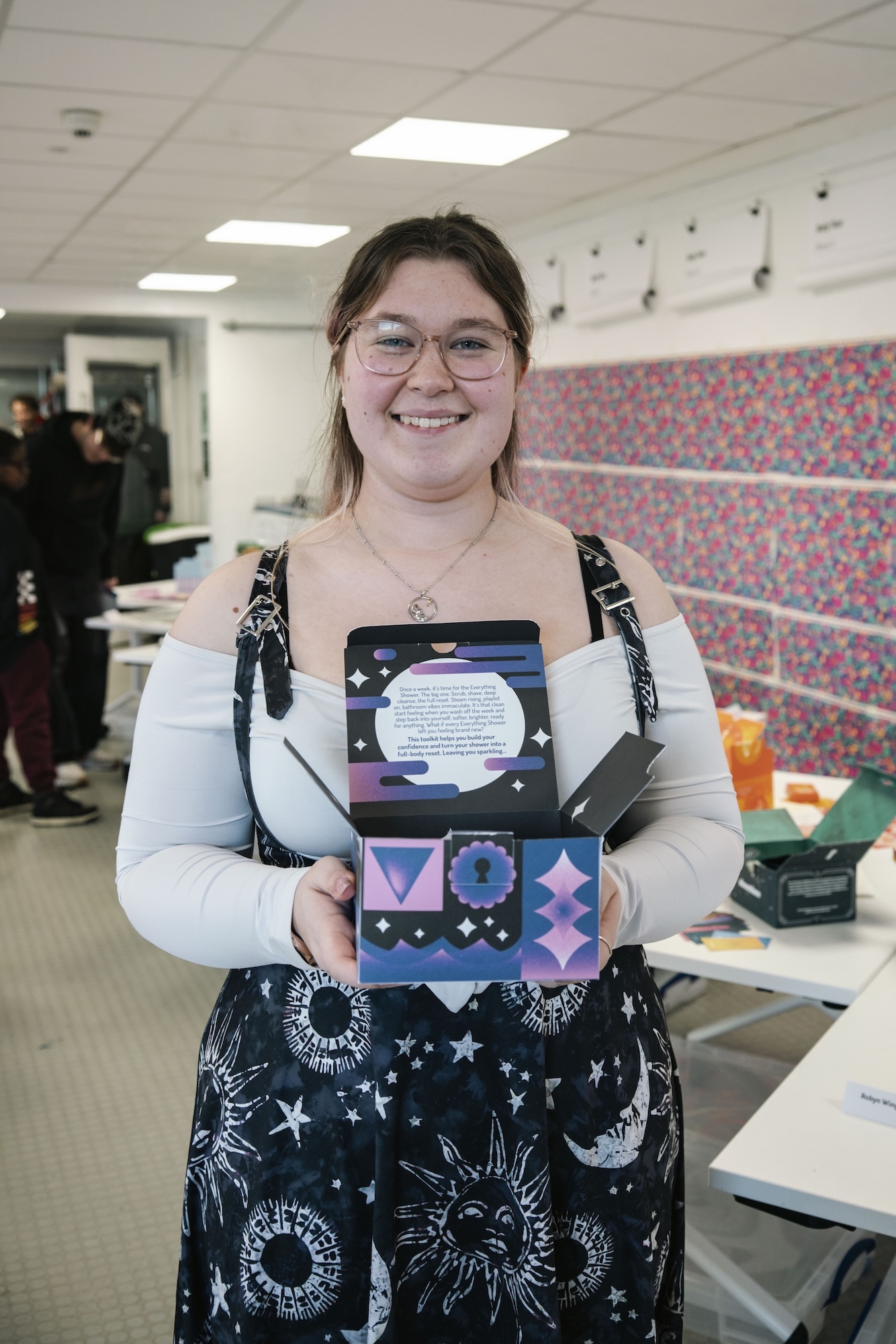 D Heywood holds colourful geometric art project in office setting with fluorescent lighting.