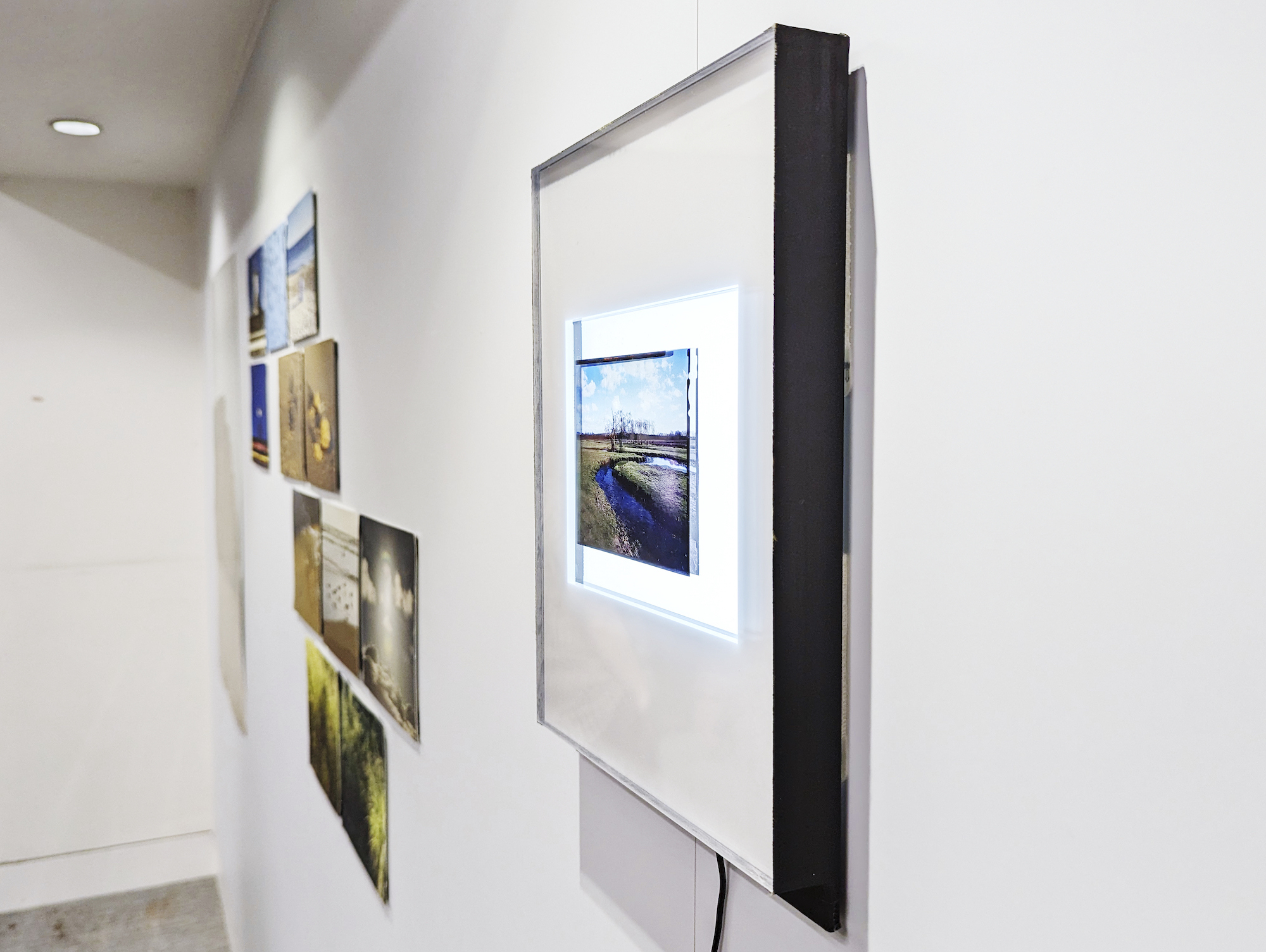 A single film photograph in a glass frame on a gallery wall. Other images are also on display further down the wall.