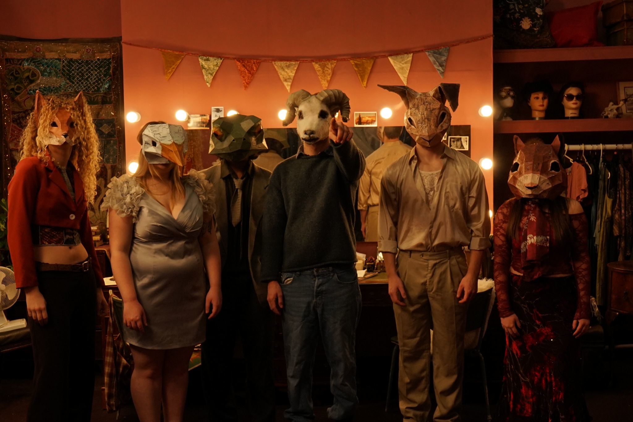 Six BA (Hons) Acting students lined up in front of a dressing room mirror each wearing a mask of the face of a different animal (a fox, a duck, a snake, a sheep, a rabbit and a squirrel).