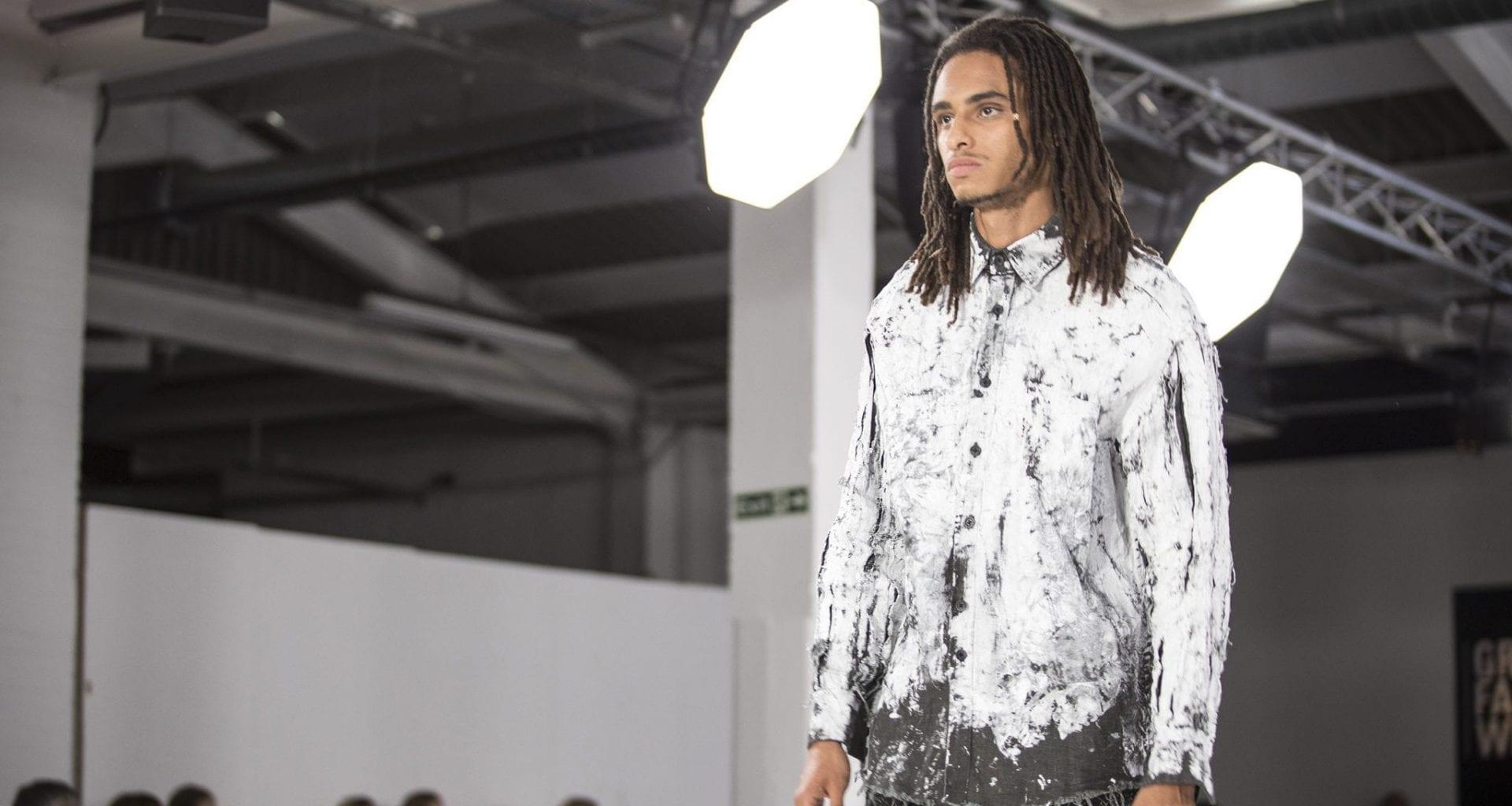 Man walking down a catwalk wearing a white and grey button-up shirt