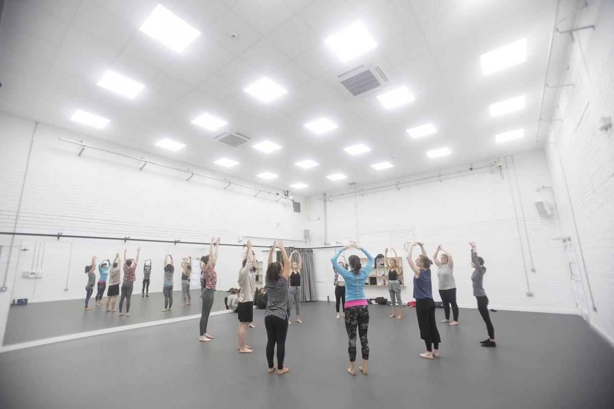 A group of dancers standing in a circle with their arms above their heads in a dance studio.