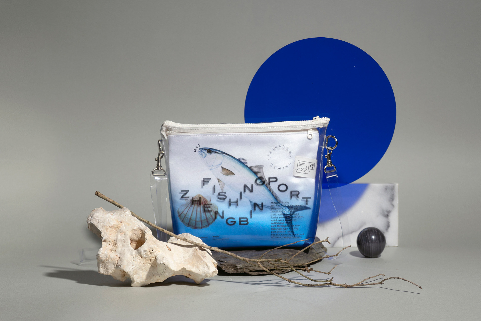 A bag with the words "Zhengbin Fishing Port" and a fish on the front, on display with a stone, a tree branch and other items.