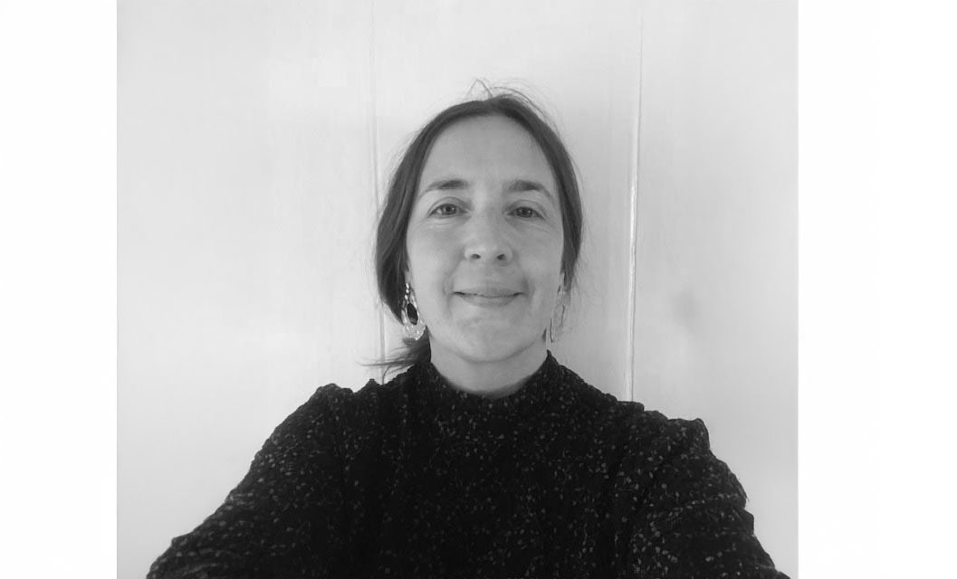Black and white portrait of woman with long dark hair wearing dark textured top, smiling at camera against white background.