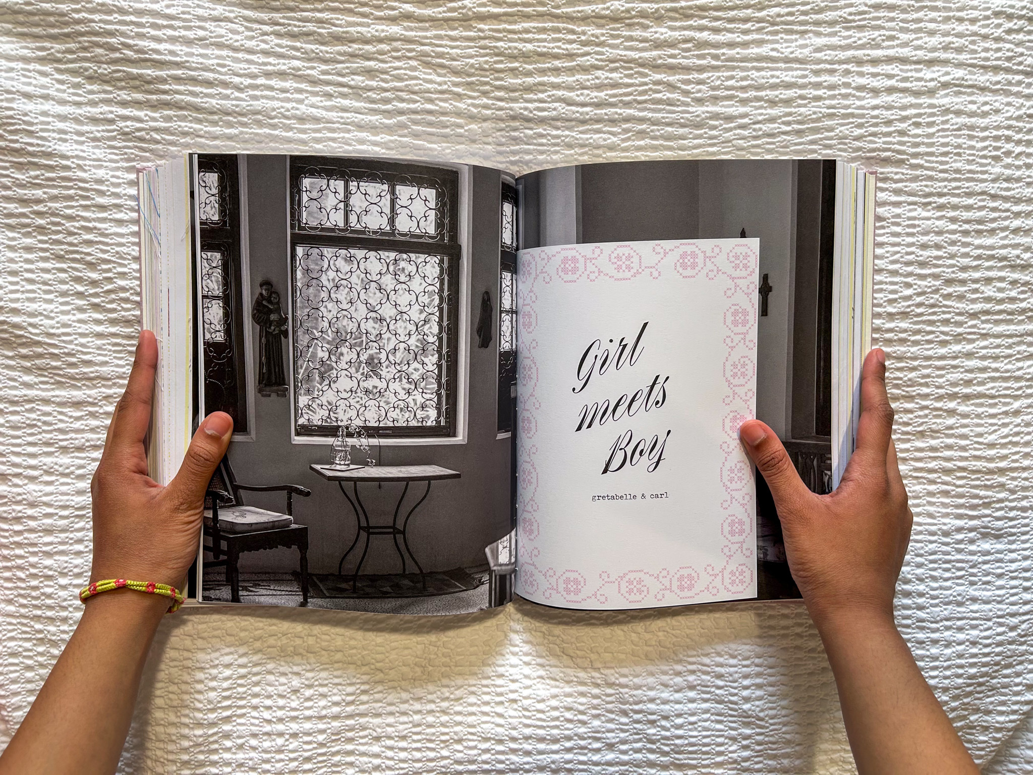 Hands holding open book showing grey interior room on left page and white page with "Girl meets Boy" text on right.