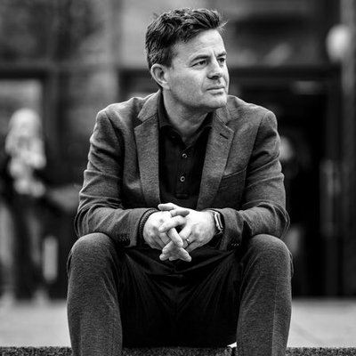 Black and white image of David McGravie sat down wearing a suit.