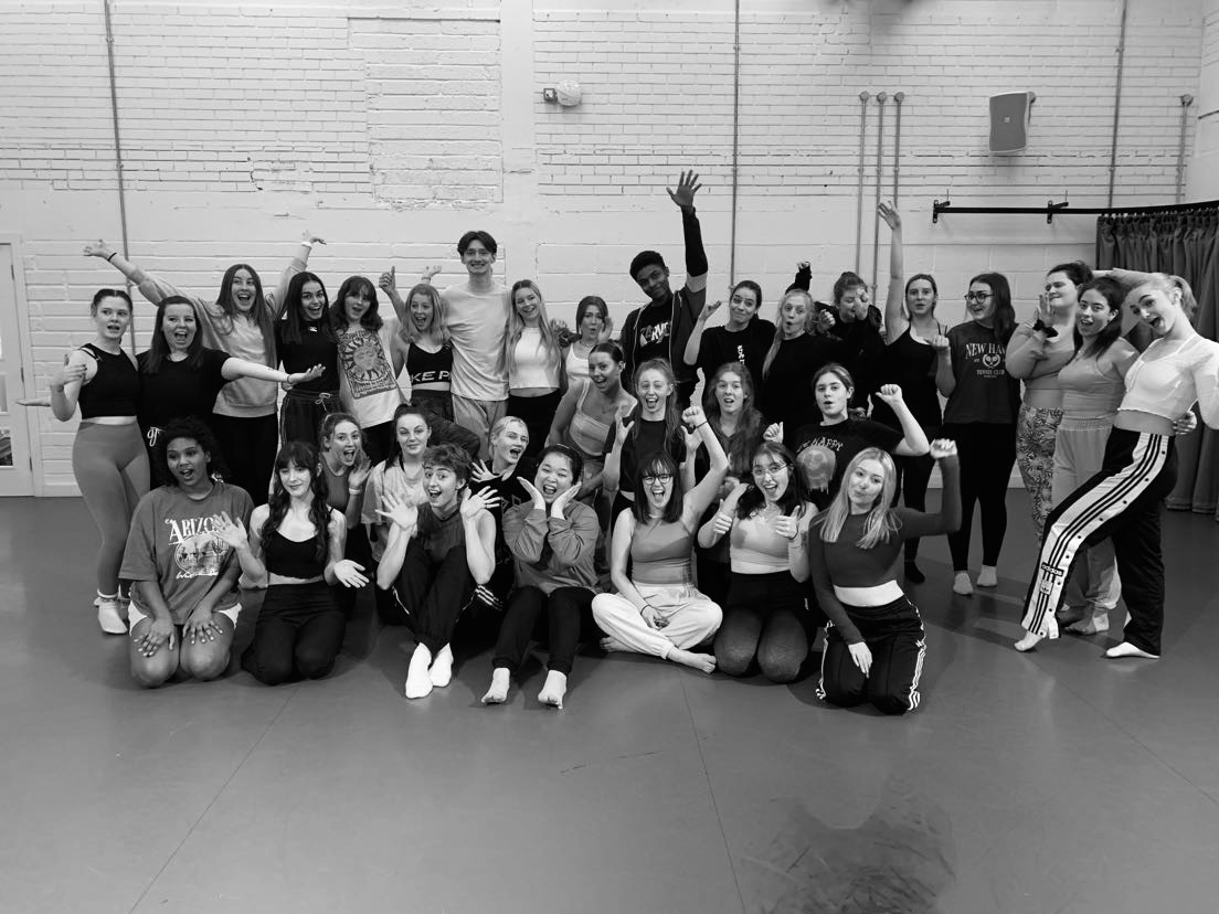 A large group of people gather and pose for a photo in a dance studio space.