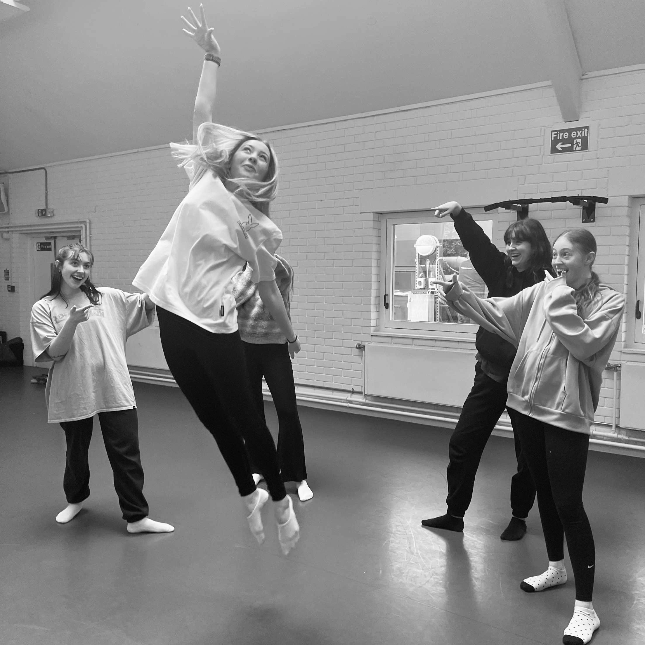 A dancer jumps up with their arm raised up like a basketballer. Four other dancers gather around them and point.
