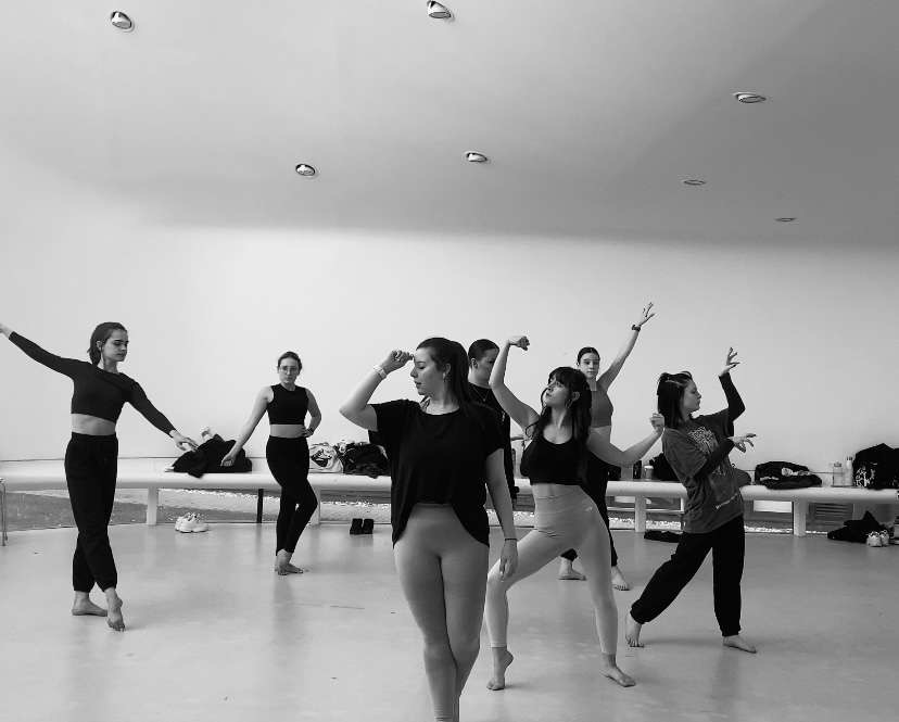 Seven dancers in the middle of a rehearsal pulling various poses in a dance studio.
