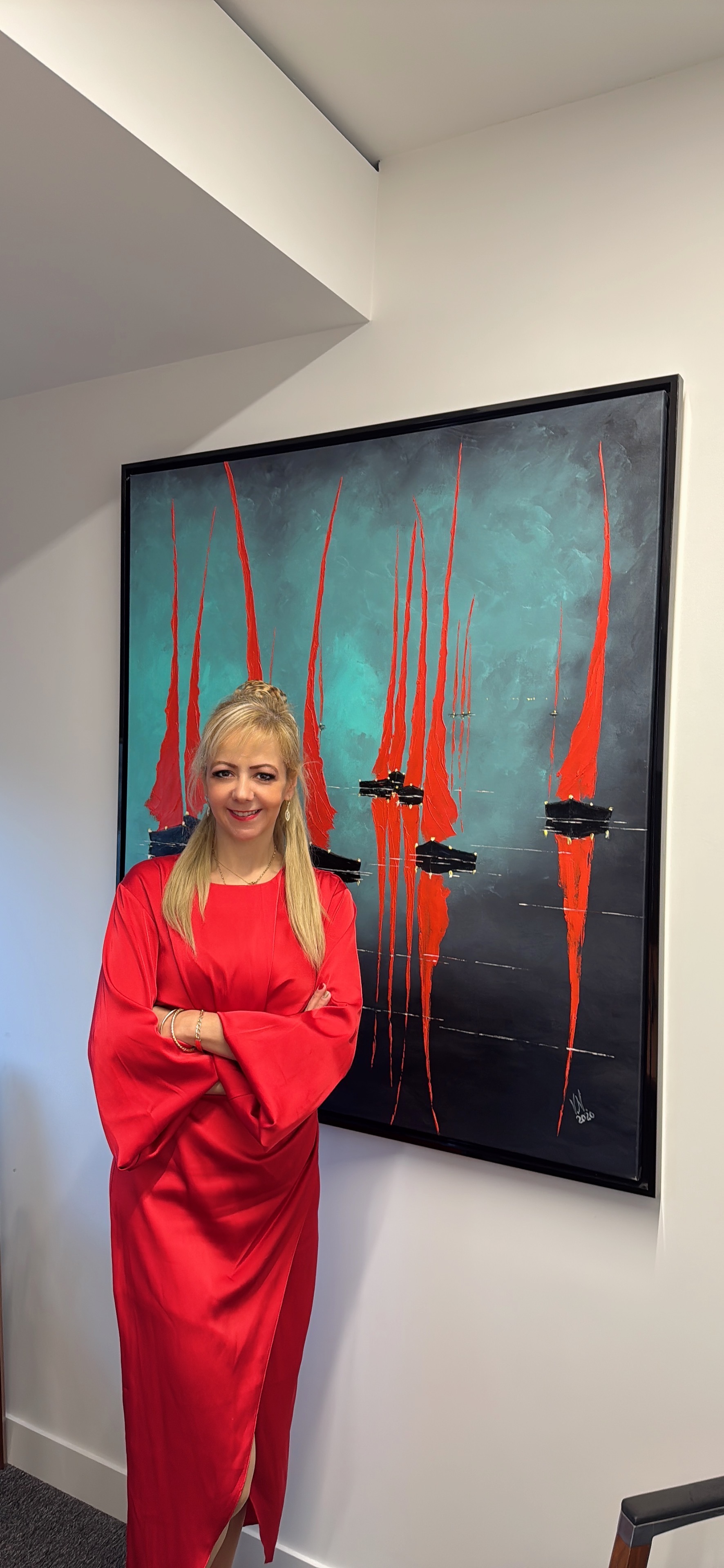 Woman in red dress standing beside framed artwork with teal background and red vertical brushstrokes on white gallery wall.