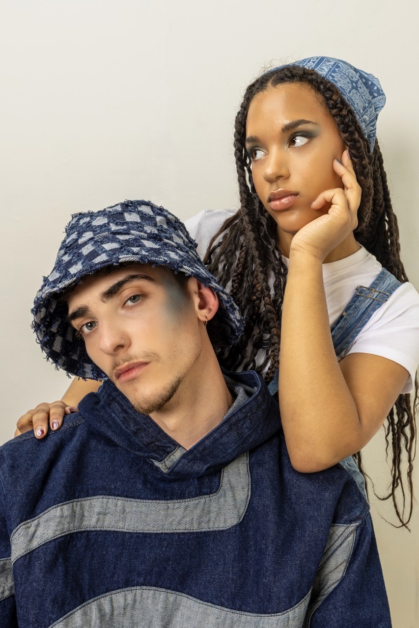 Two people wearing matching blue denim bucket hats and striped clothing, both with hands positioned near their faces in contemplative poses.