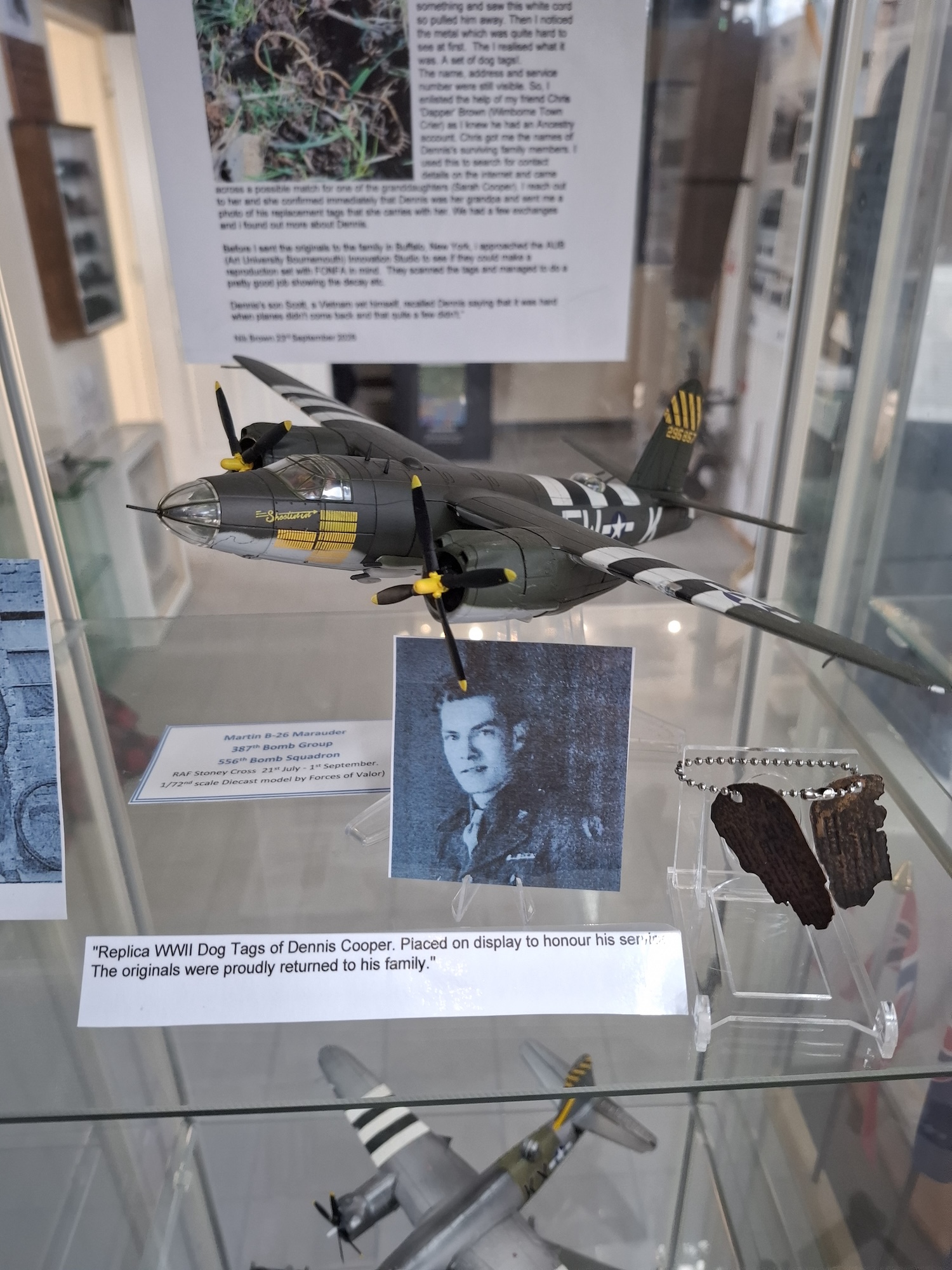 A replica World War II dog tag display featuring a model aircraft, a portrait of Dennis Cooper and his dog tags in a glass cabinet.