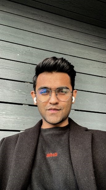 A headshot of D Trivedi against a grey wooden panelled background