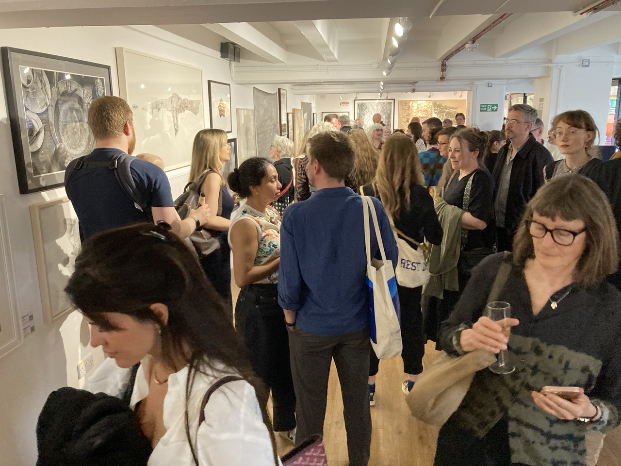Visitors walking round the Derwent Art Prize exhibition, tote bags and drinks in hand.