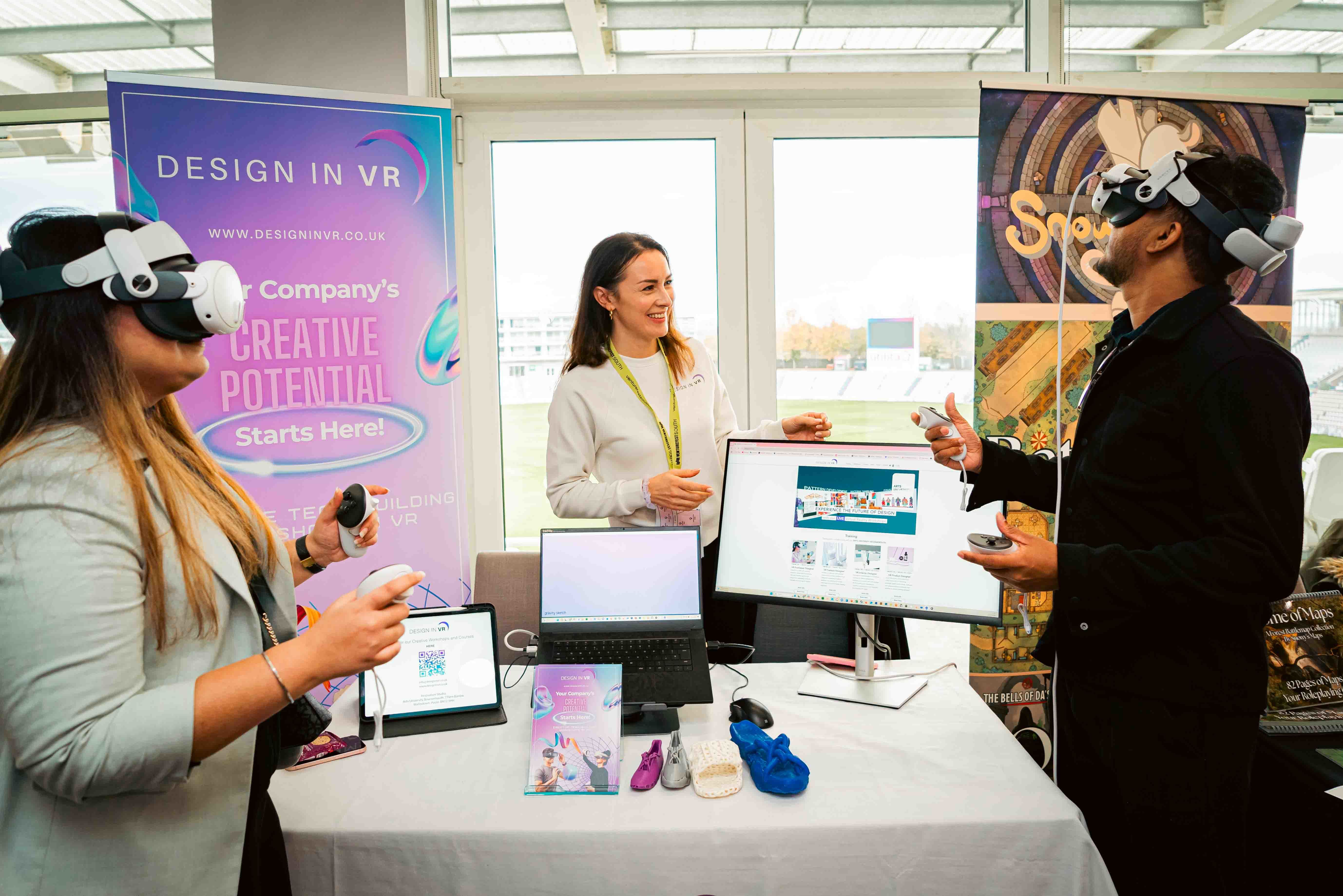 E Savosina at her stall for 'Design in VR' at Venturefest South 2024, watching as two attendees use VR headsets and controls.