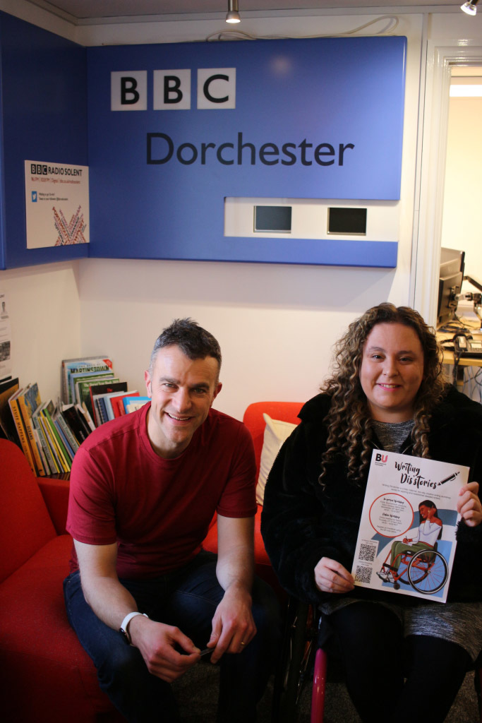 Two participants of the Writing Dis'stories sessions, sat below a 'BBC Dorchester' sign.