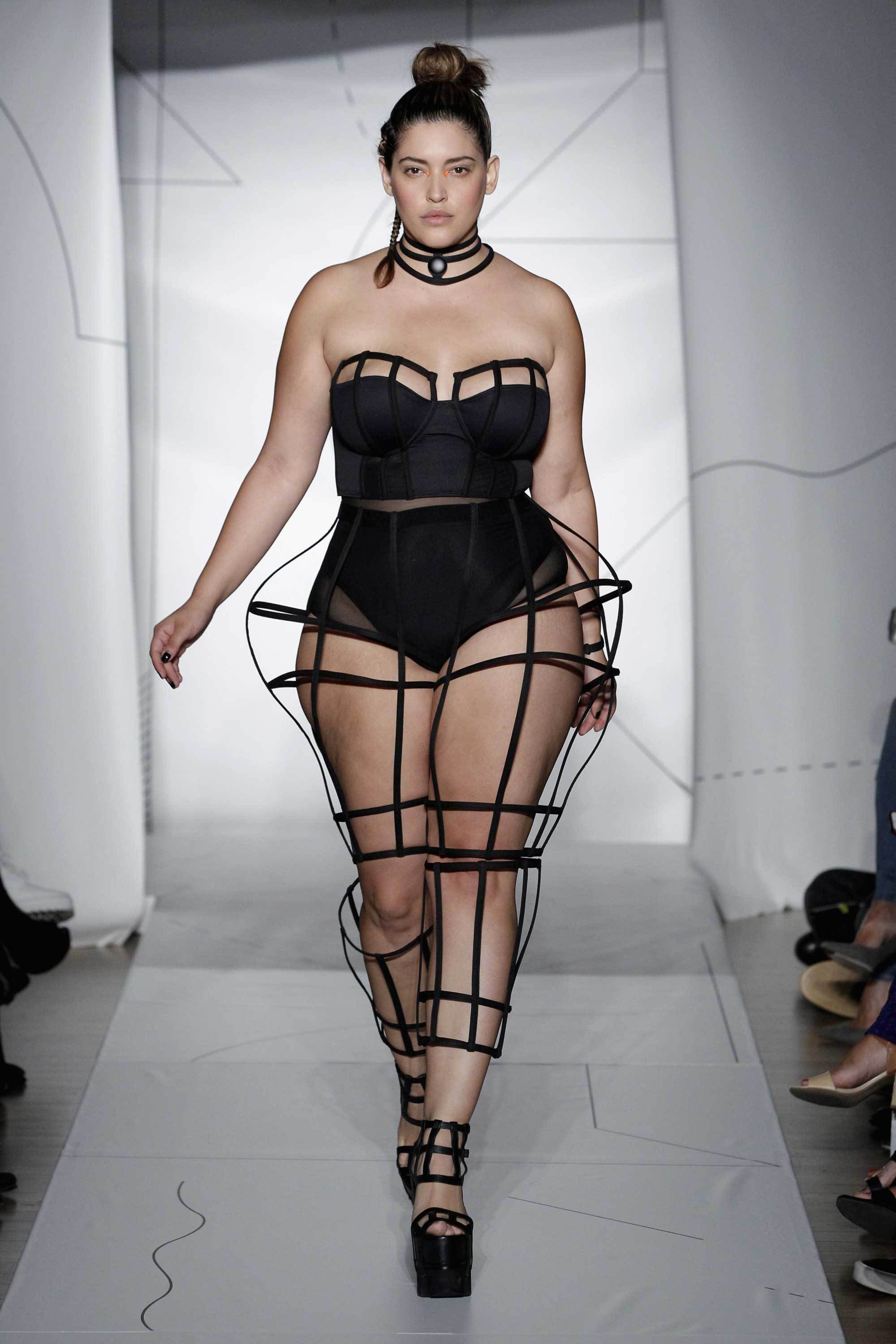 Model in a bodice and netted leggings walks down a runway.