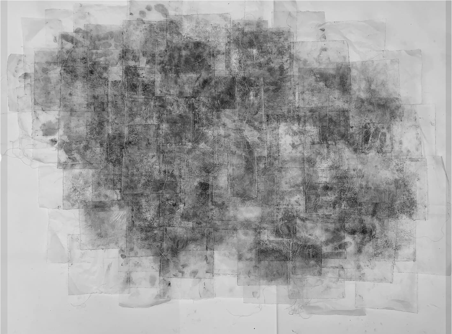 Abstract charcoal drawing with dark grey smudged marks concentrated in centre, fading to lighter grey washes towards edges on white paper.