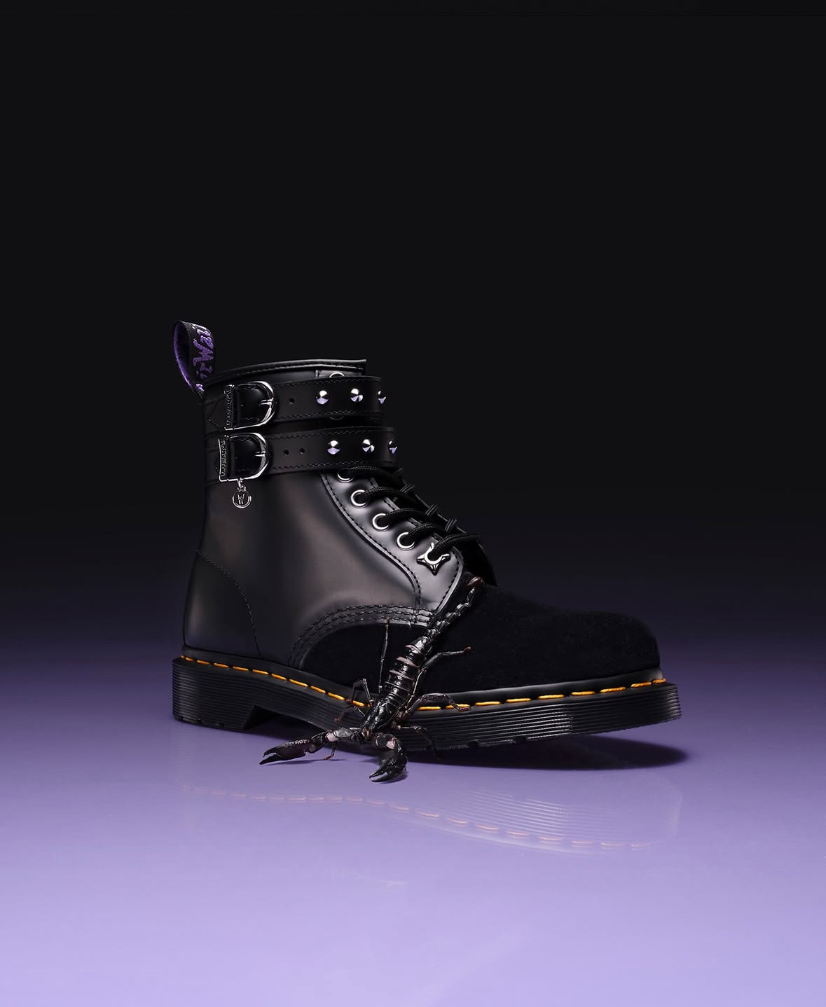 Black leather boot with metal buckles and laces on purple gradient background fading to black above.