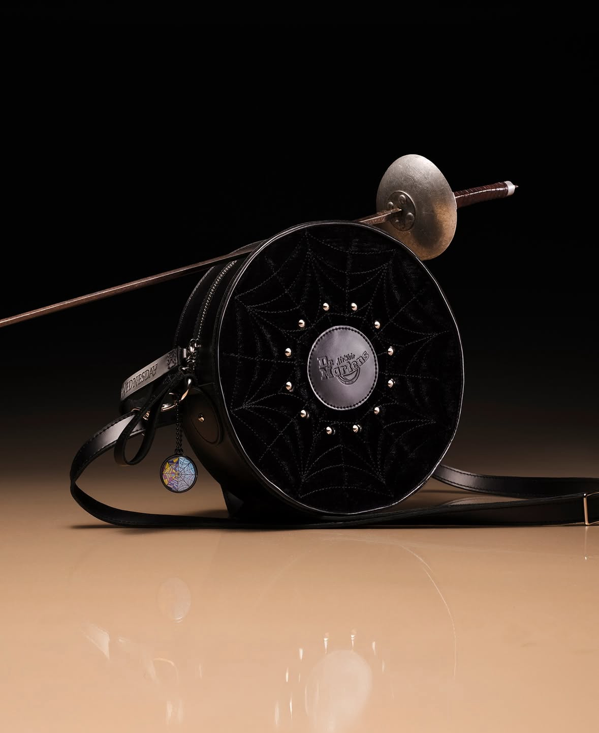 Black fishing reel with metal components and line guide, positioned on beige surface against dark background.