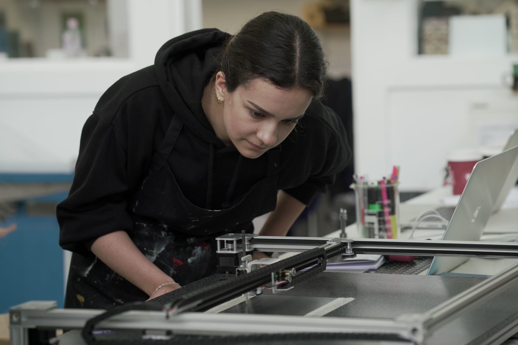 Person leaning over a drawing machine as it is in use.