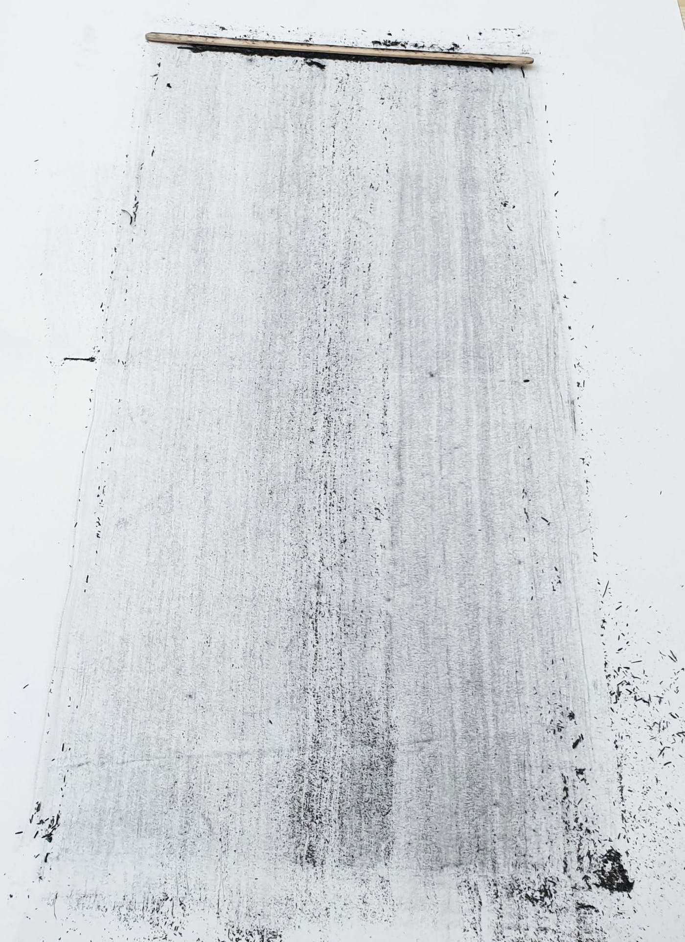 A thin wooden tool at the top of a page with lines black powder scraped behind it.