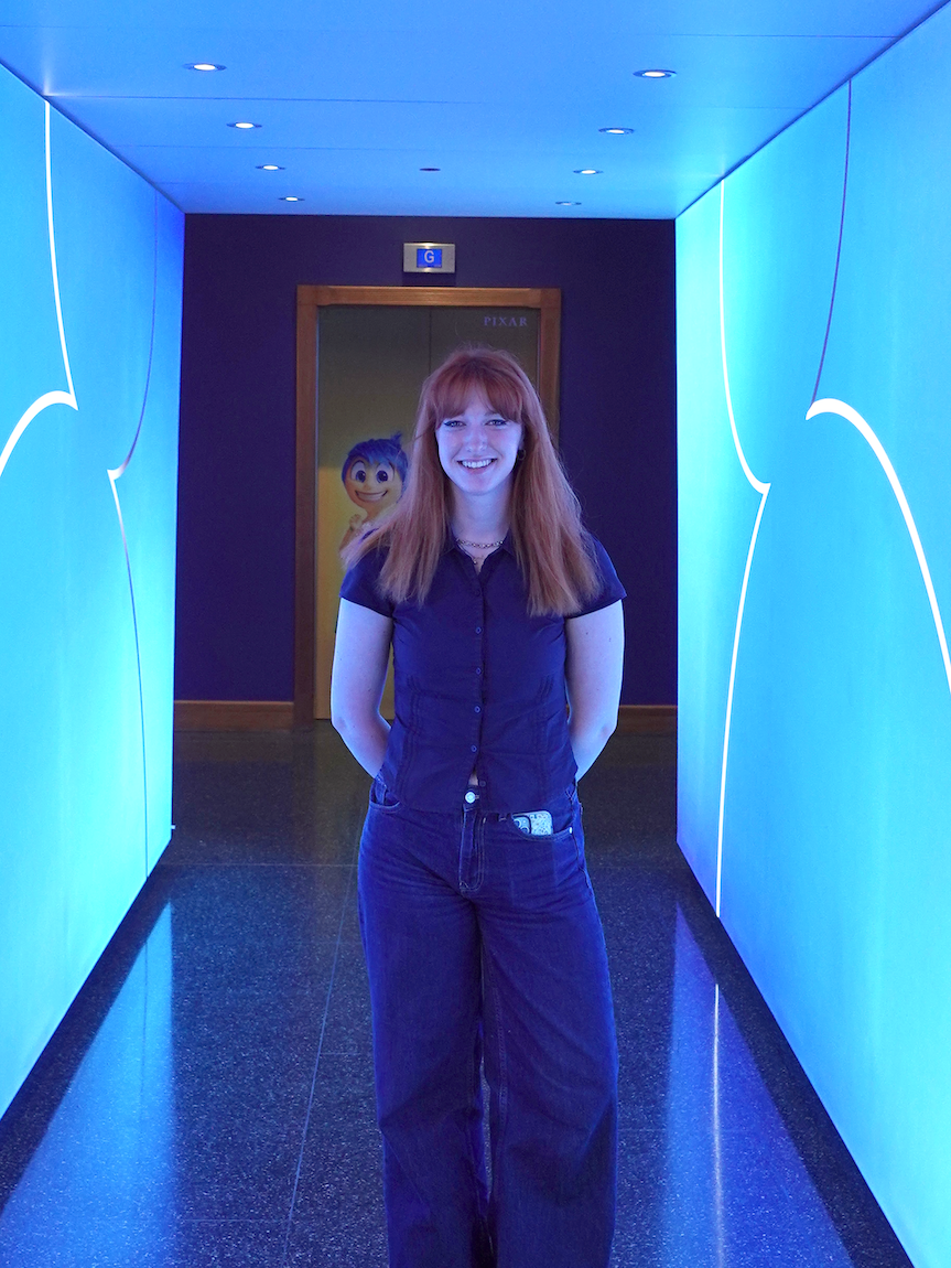 E Jarvis standing in corridor with blue LED lighting and angular white wall panels. A cutout of Joy from Pixar's "Inside Out" is visible in the background.
