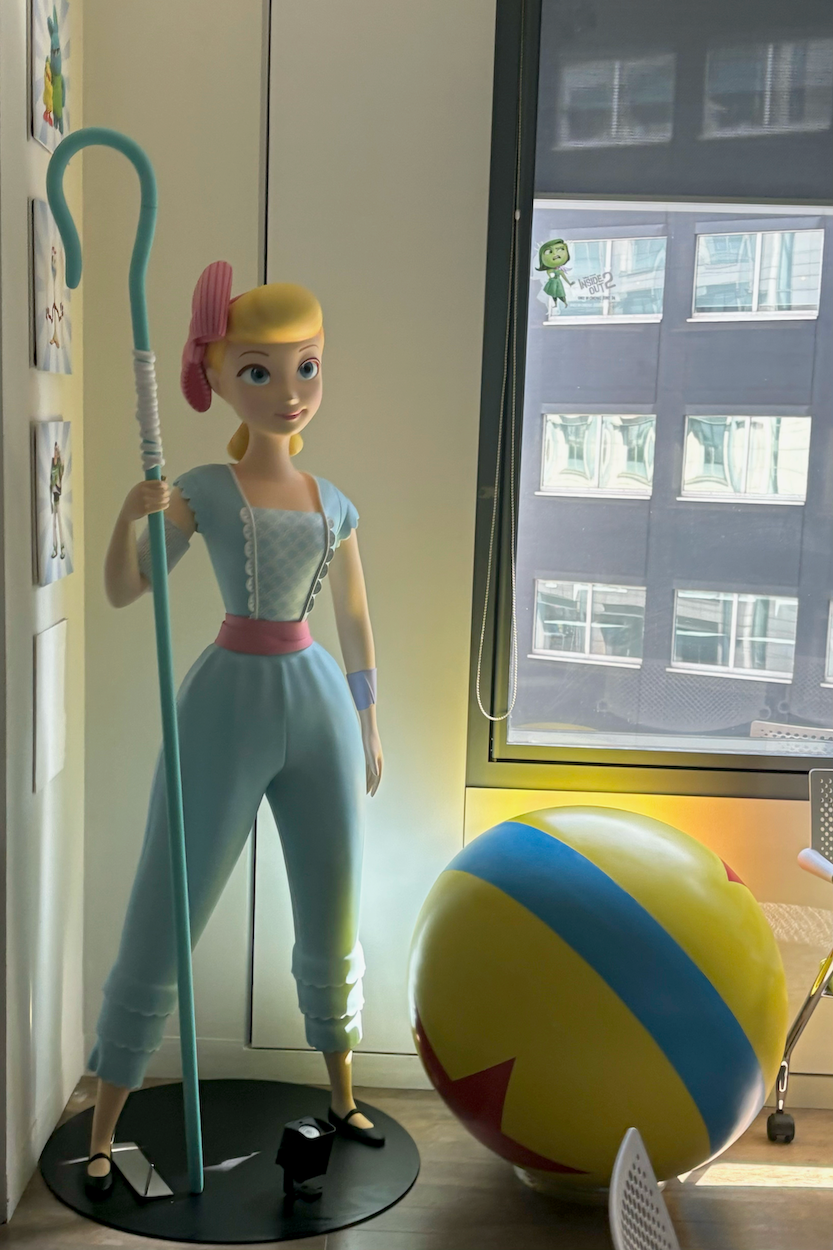Large figurine of Bo Peep from the Toy Story franchise, beside large striped ball near window in bright room.