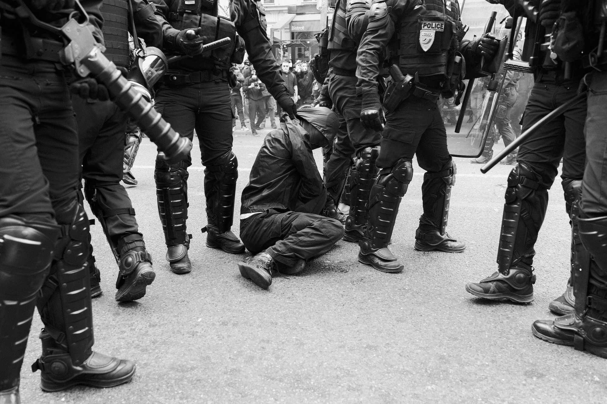 A protestor dressed in black is held on the ground surrounded by armoured riot police.