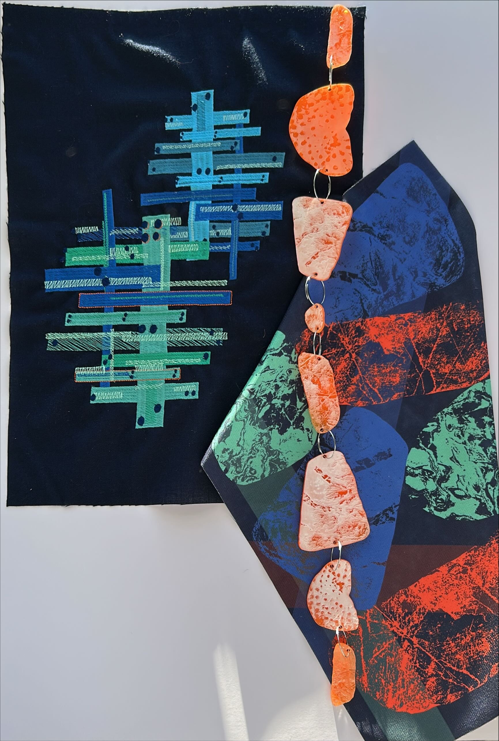 Close-up of a piece of textiles design work with a fabric sample on display on a white gallery wall.