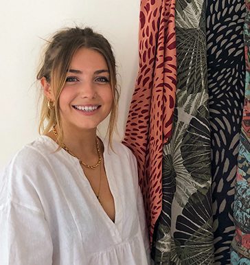 Headshot of Textiles graduate L Kretowicz, standing next to several textiles samples