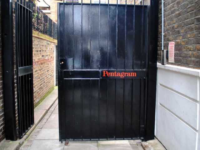 A pair of large black gates, one of which is open. The other is shut and has the word 'Pentagram' on the front of it.