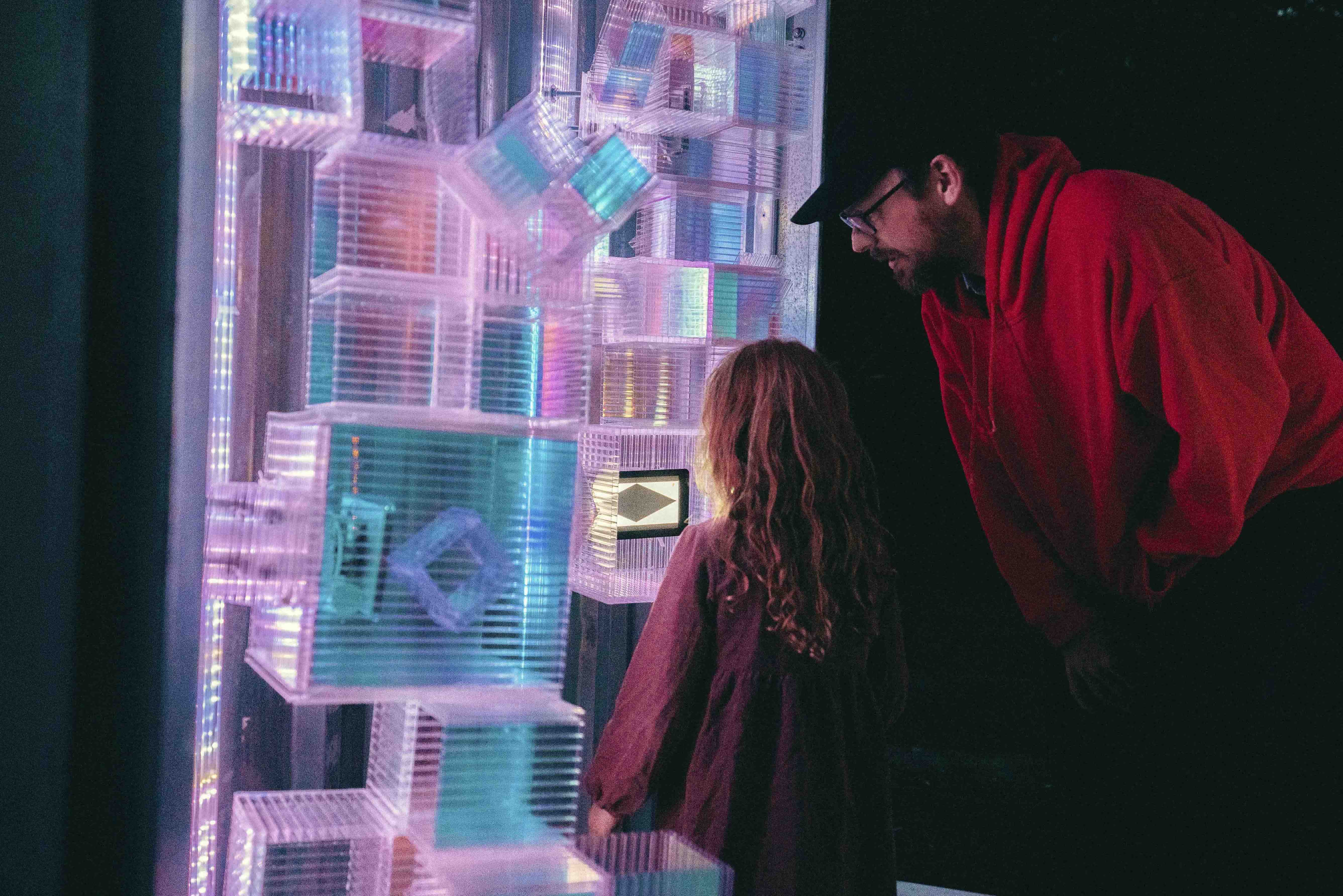 Two people stand and look at a collection of lit-up transparent boxes stacked on top of one another.