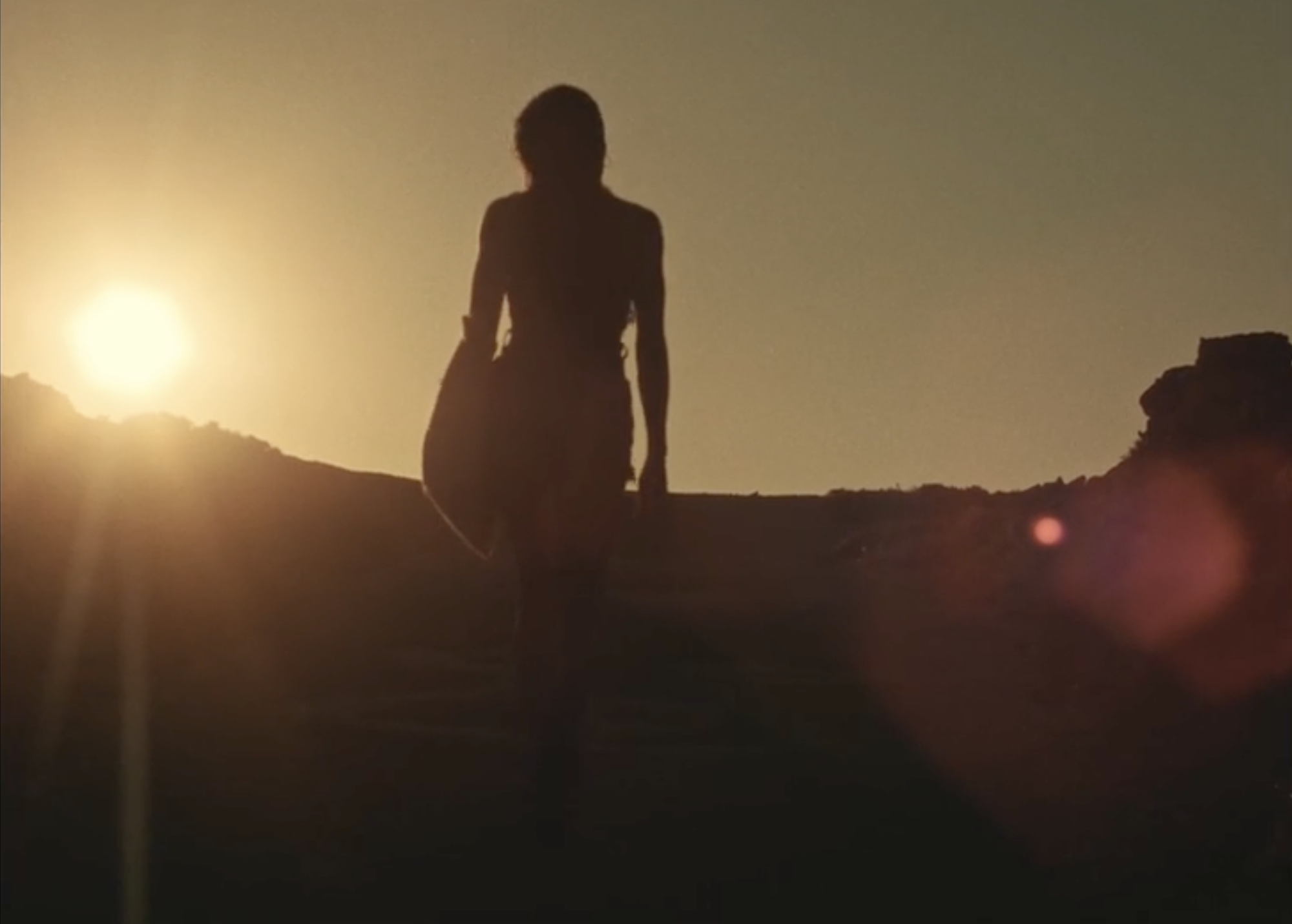 Film still of a young person's silhouette walking towards the camera, with glaring sunshine in the background.