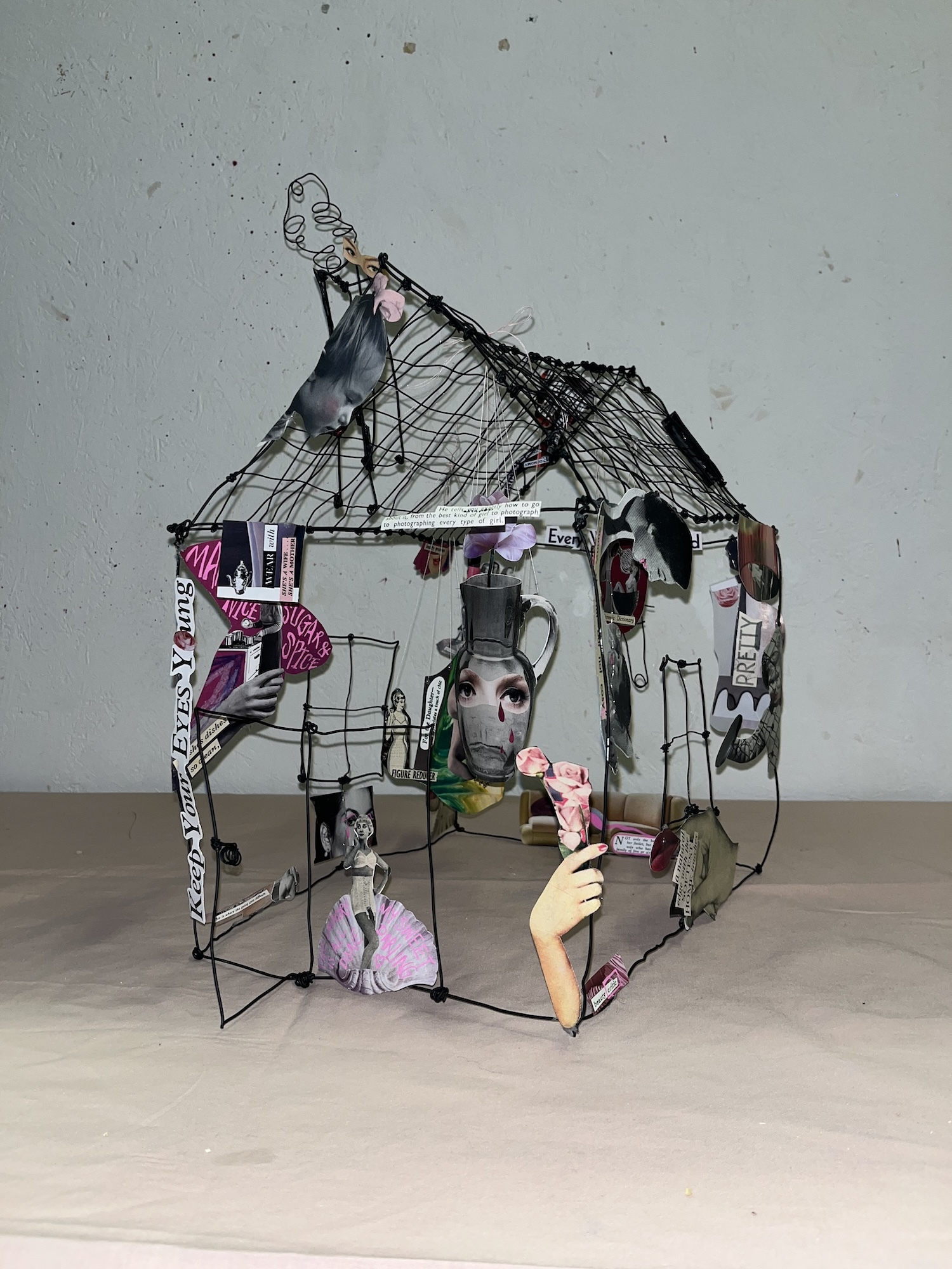 Wire sculpture of a house with cut-out scraps from various magazines and print publications stuck in places.