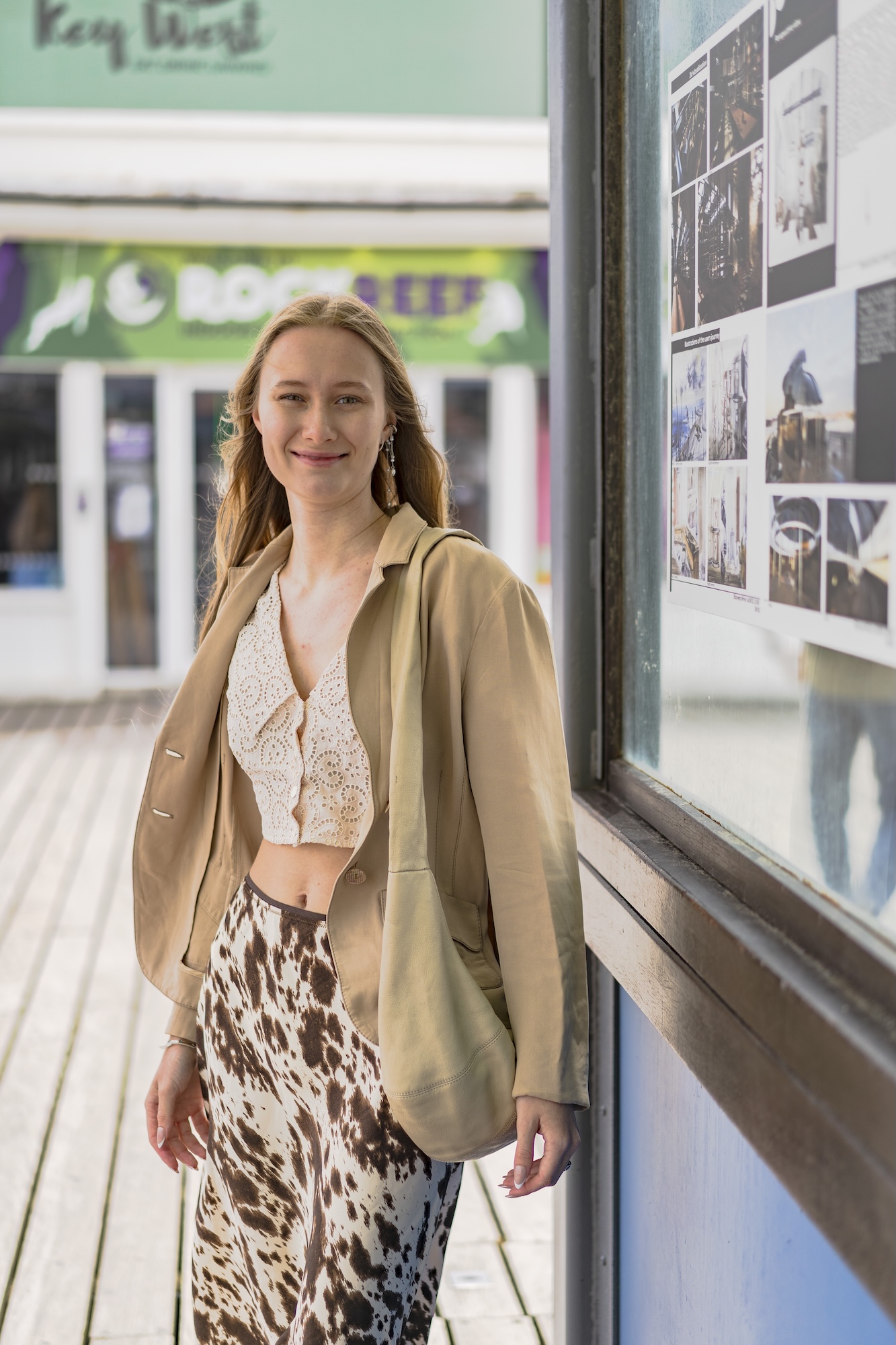 Portrait of E Rimar standing next to a display board on Bournemouth Pier containing a poster.