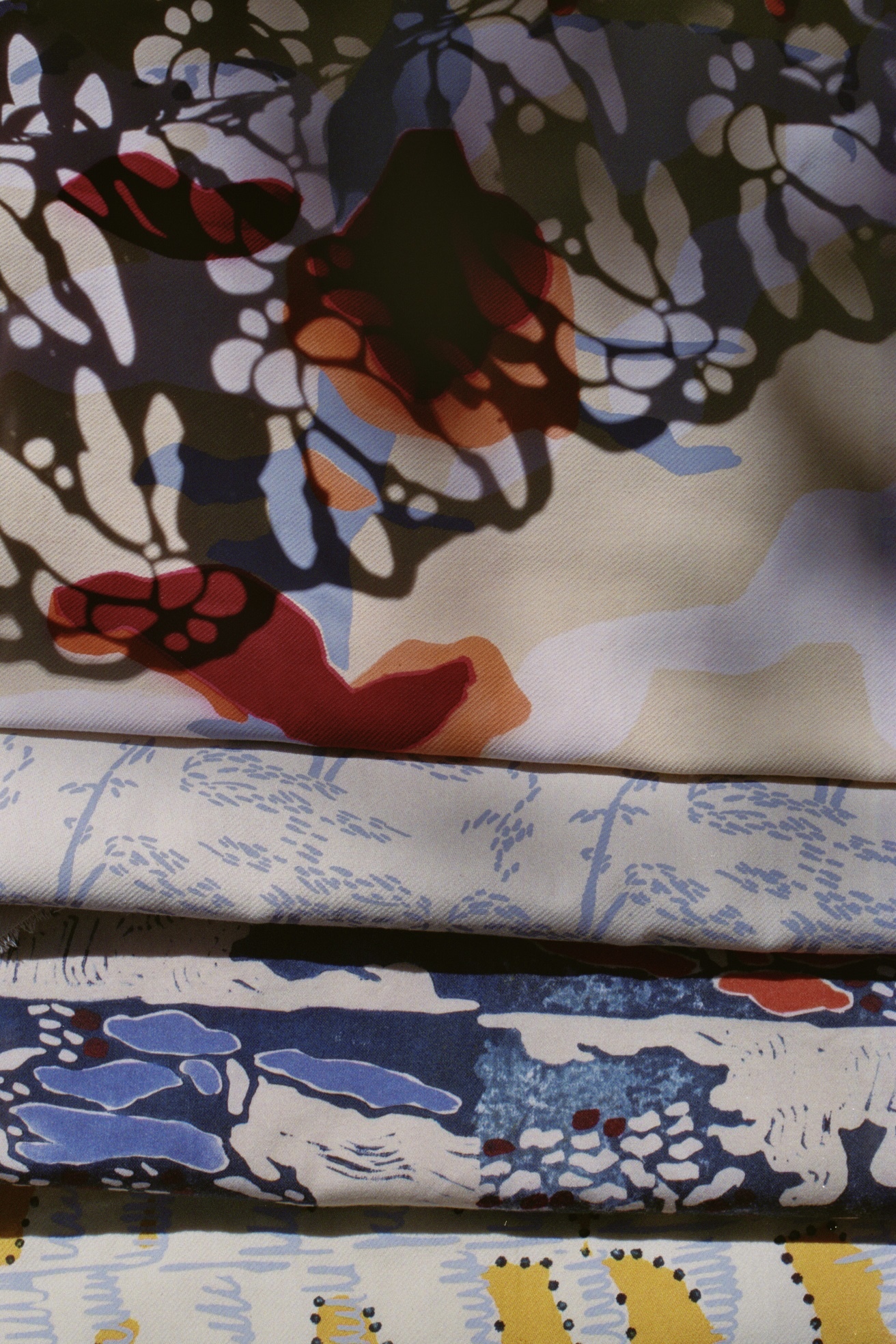 Five samples of colourful patterned and embroidered fabric, stacked on top of one another.