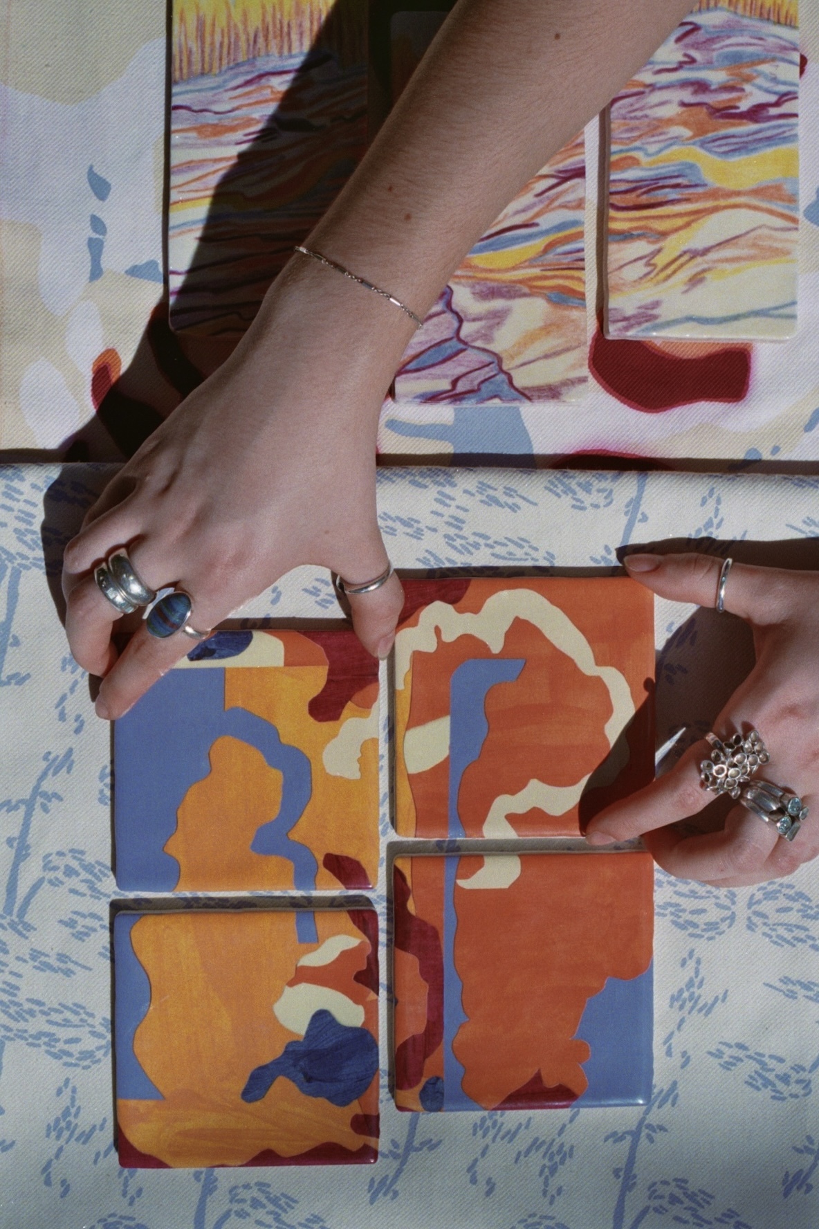 A person's hands arranging a set of coloured tiles. The tiles show a colourful abstract pattern.