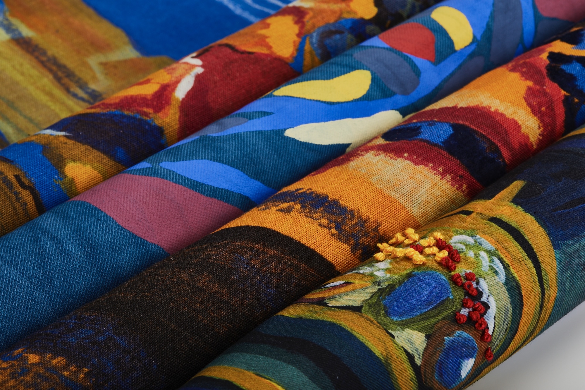 Four rolls of colourful patterned fabric lying next to each other.