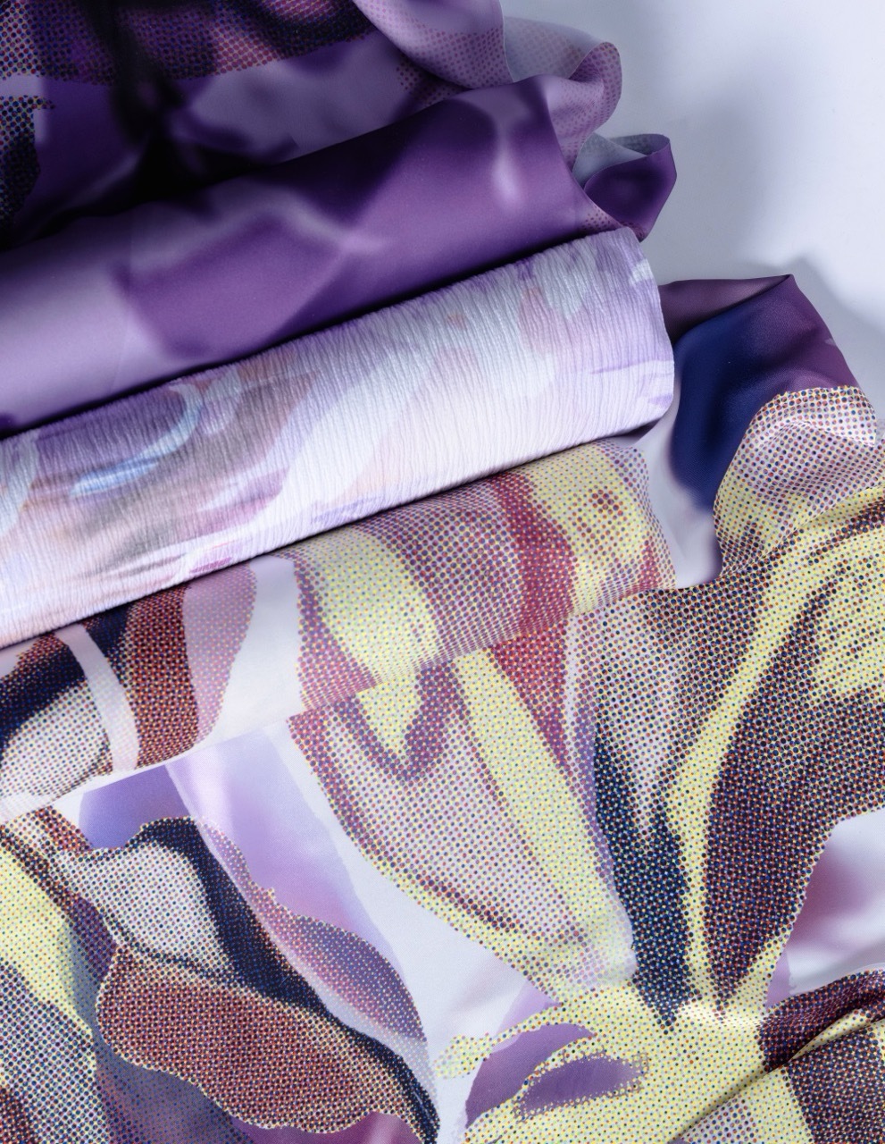 Layered fabrics in purple, white, and yellow with dotted halftone patterns and flowing translucent ribbons creating an abstract composition.