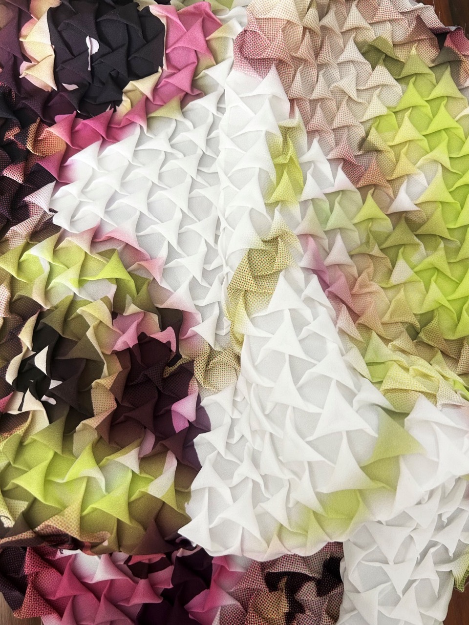 Layered fabric petals in white, pink, yellow, green and dark purple arranged in dense ruffled clusters across the frame.