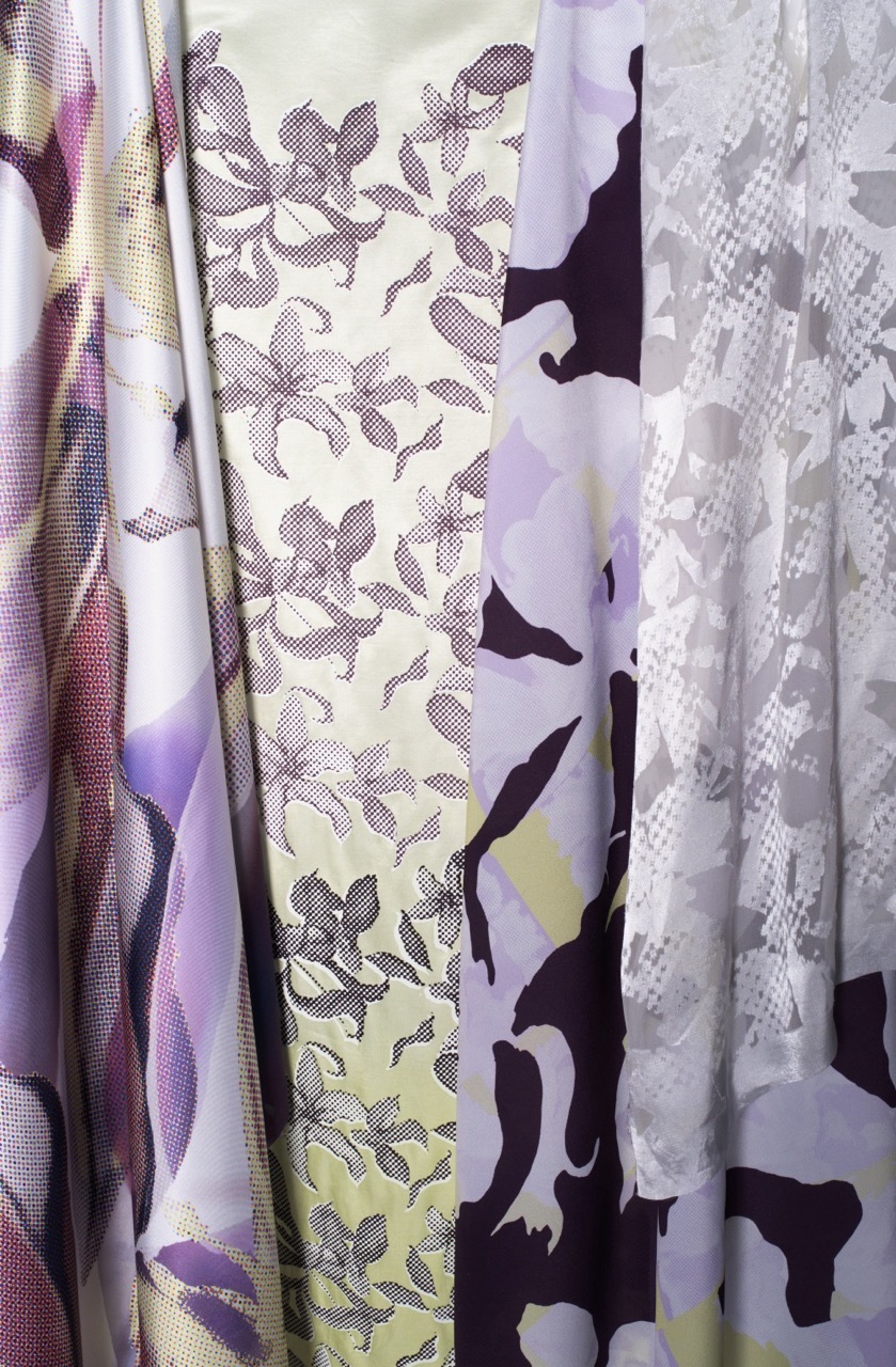 Layered fabrics with purple, white, and black patterns including floral prints, geometric shapes, and solid colour blocks in vertical folds.