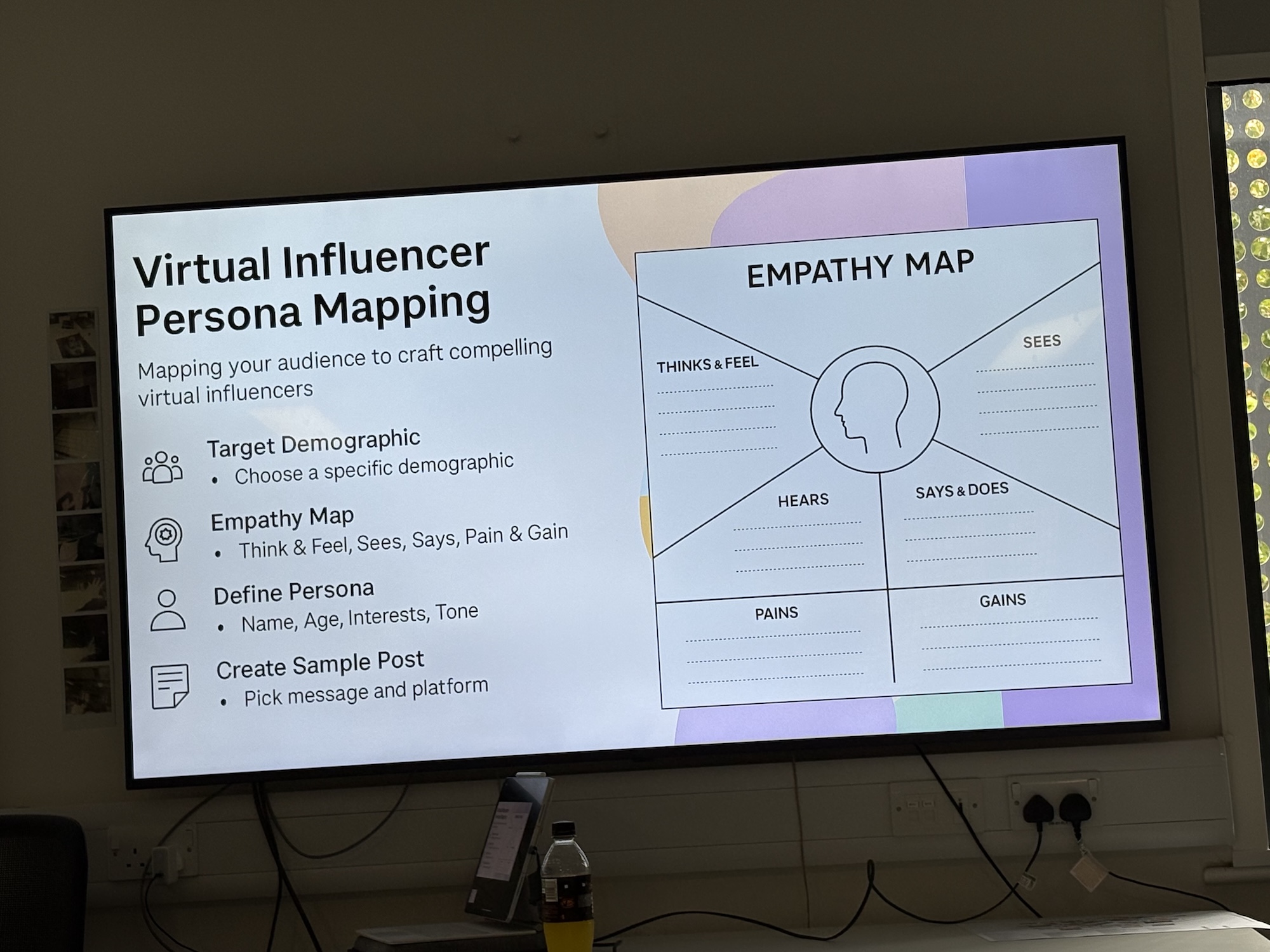 A wall-mounted monitor displays a slide titled “Virtual Influencer Persona Mapping” with an empathy map diagram, beside a white panel listing target demographic, define persona and create sample post.