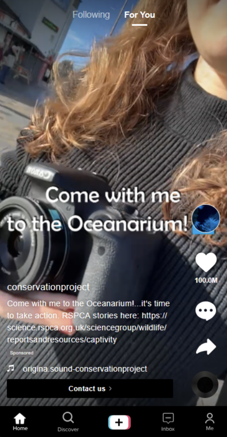 A close-up of a person holding a Canon camera, with brown hair and a black ribbed top, overlaid with the text “Come with me to the Oceanarium!” and a heart icon.